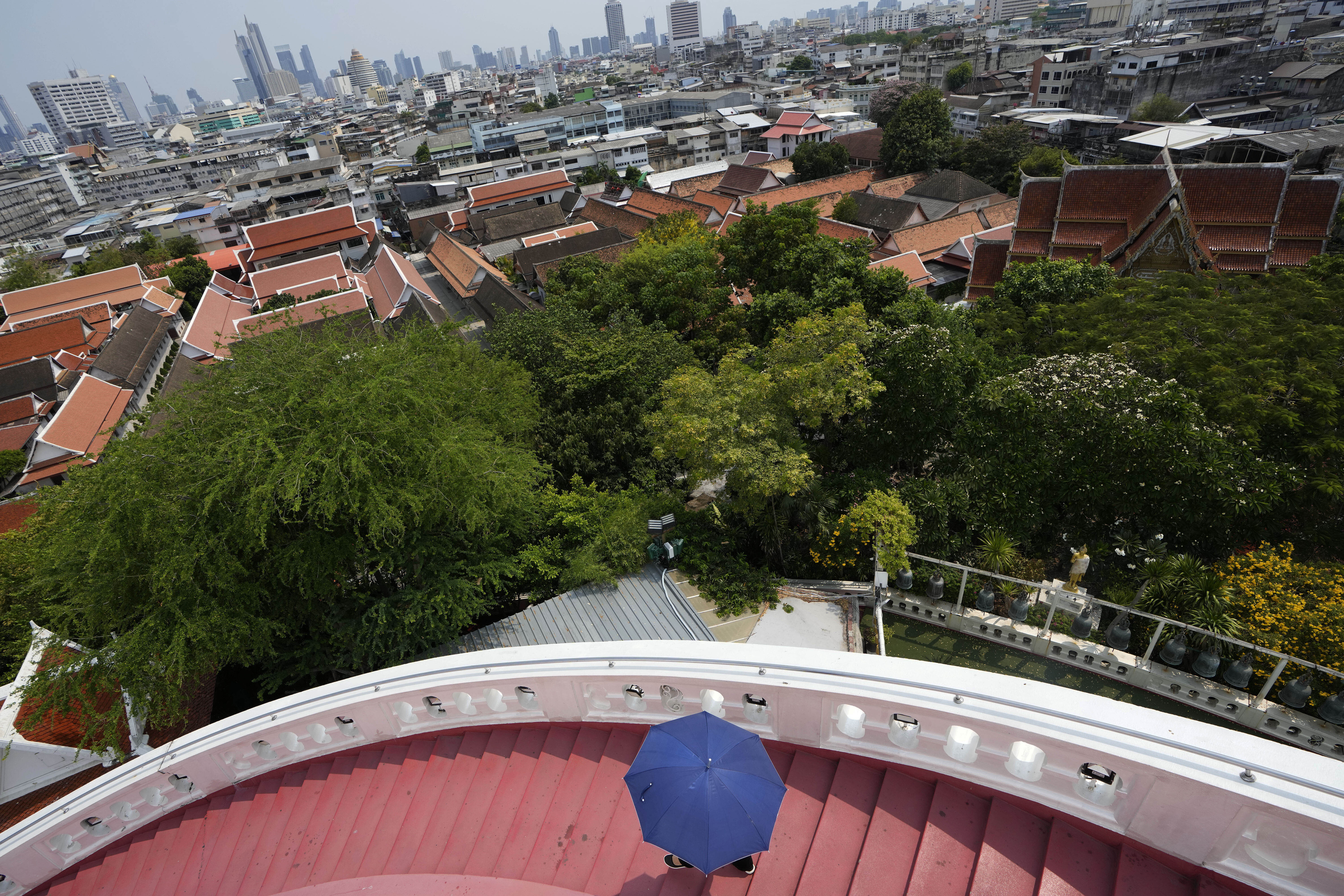 A visitor with an umbrella walks downstairs of the Golden Mount inside the Buddhist Wat Saket temple complex in Bangkok, Thailand, Tuesday, April 9, 2024. Thailand, Cambodia and other countries in this region are celebrating with their annual water festivals as they also suffer through the global heat wave. (AP Photo/Sakchai Lalit)