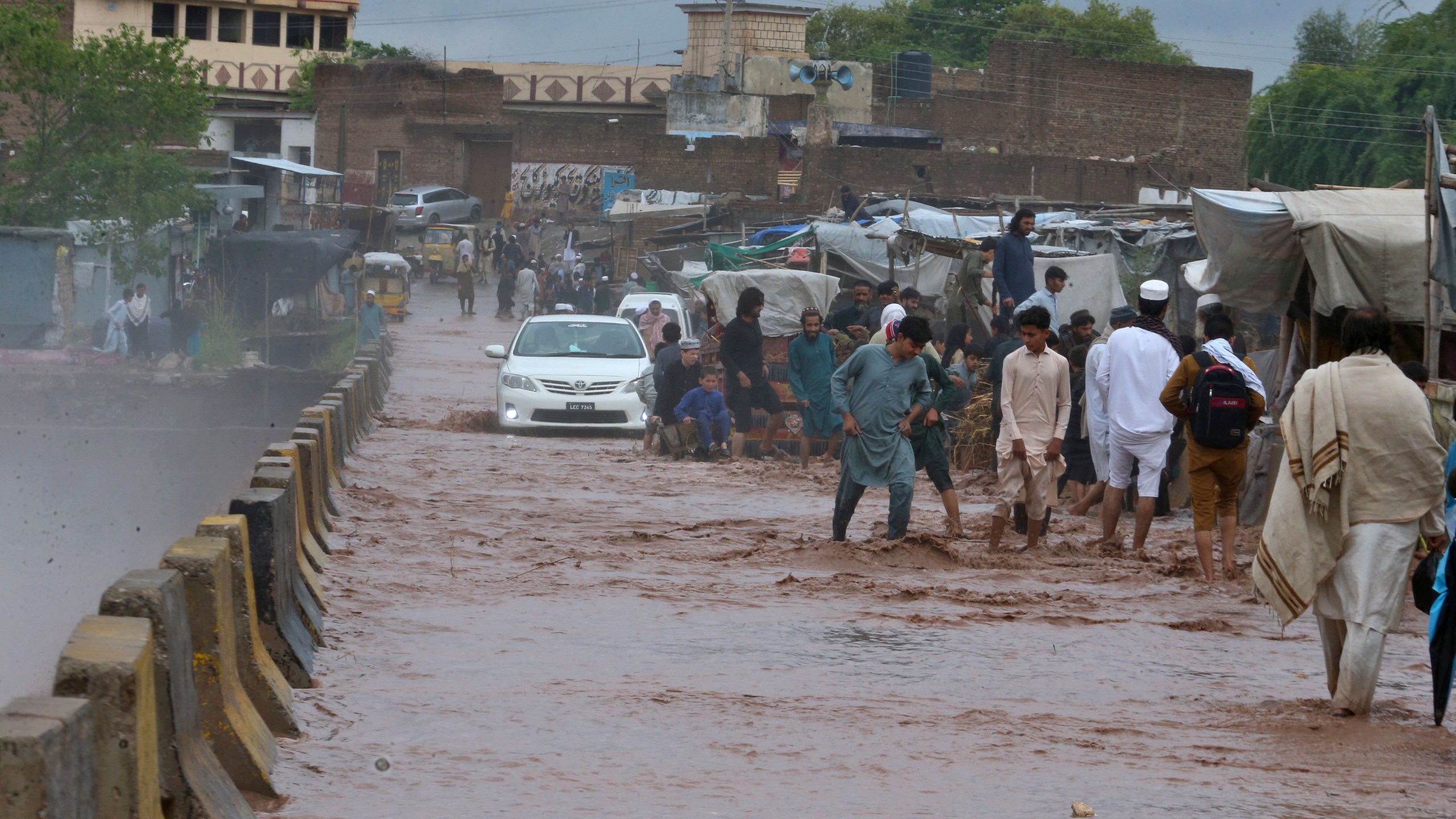 People wade through a flooded bridge on a stream, which is overflowing following heavy rains, on the outskirts of Peshawar, Pakistan, Monday, April 15, 2024. Lightnings and heavy rains killed dozens of people, mostly farmers, across Pakistan in the past three days, officials said Monday, as authorities declared a state of emergency in the country's southwest following an overnight rainfall to avoid any further casualties and damages. (AP Photo/Muhammad Sajjad)