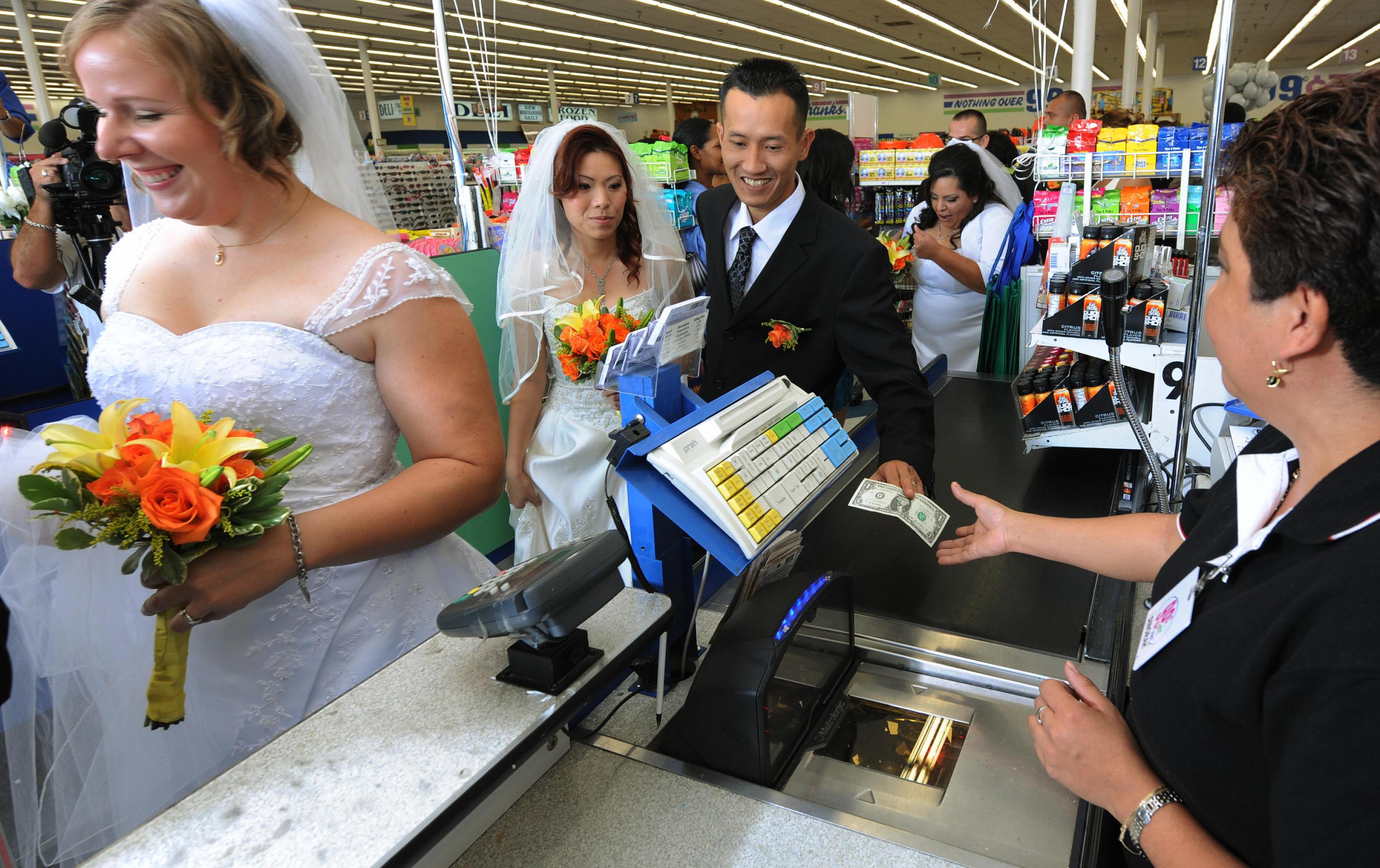 Bonnie Cam and Jon Nguyen pay for their 99 cent wedding ceremony at a checkout at the 99 cent store in Los Angeles on September 9, 2009. The budget supermarket chain helped nine happy California couples beat the recession blues by offering cut-price wedding ceremonies -- for just 99 cents each. The 99 Cents Only Stores chain is picking up the tab for nine couples at its branch on Sunset Boulevard in the heart of Hollywood on Wednesday to mark the ninth day of the nine month in 2009. After getting hitched, the nine couples were handed 99 dollars and 99 cents in cash before being whisked off to an undisclosed "famous romantic Los Angeles" location. AFP PHOTO/Mark RALSTON (Photo credit should read MARK RALSTON/AFP via Getty Images)