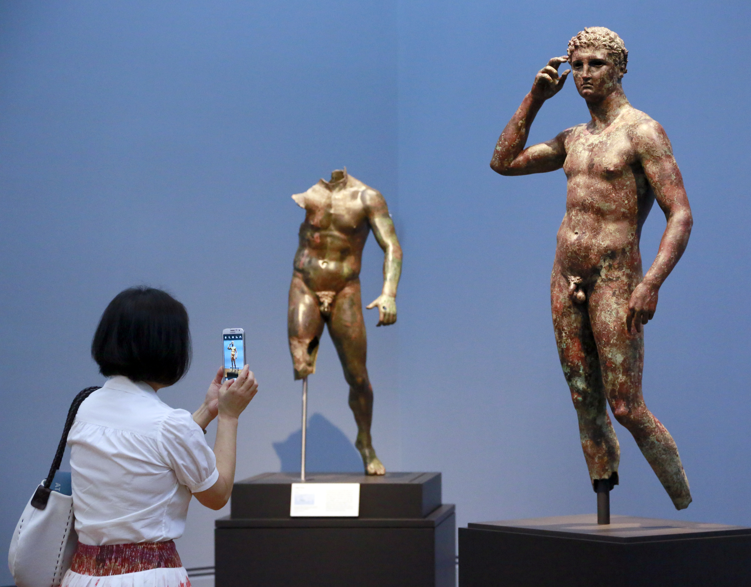 FILE - Reporter Sookee Chung takes a photo of a sculpture titled "Statue of a Victorious Youth, 300-100 B.C." at the J. Paul Getty Museum in Los Angeles, on July 27, 2015. A European court upheld Italy’s right to seize a prized Greek statue from the J. Paul Getty Museum in California, rejecting the museum’s appeal on Thursday and ruling Italy was right to try to reclaim an important part of its cultural heritage. (AP Photo/Nick Ut, File)
