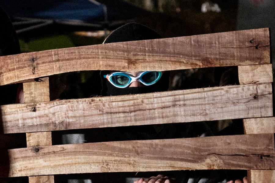 A pro-Palestinian protester takes shelter behind a barricade amid clashes at a pro-Palestinian encampment set up on the campus of the University of California Los Angeles (UCLA), in Los Angeles on May 1, 2024.