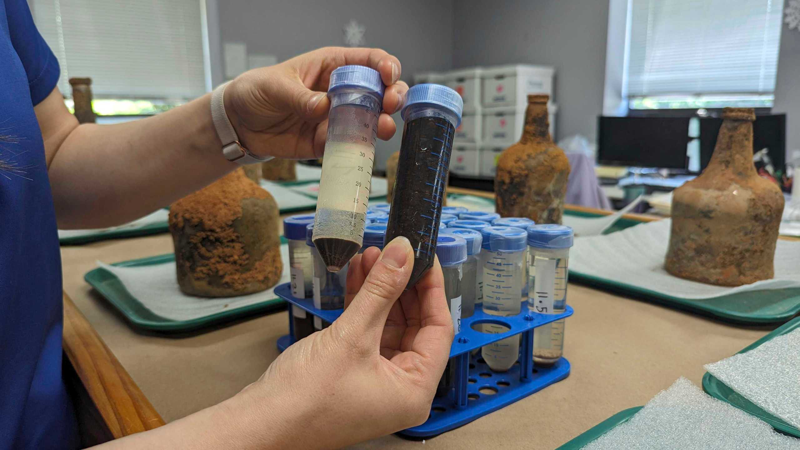 Curator Lily Carhart holds up different samples of liquid they extracted from a few dozen 18th-century glass bottles that contained fruit after they were unearthed from the cellar of George Washington's residence in Mount Vernon, Va., Monday, June 17, 2024. (AP Photo/Nathan Ellgren)