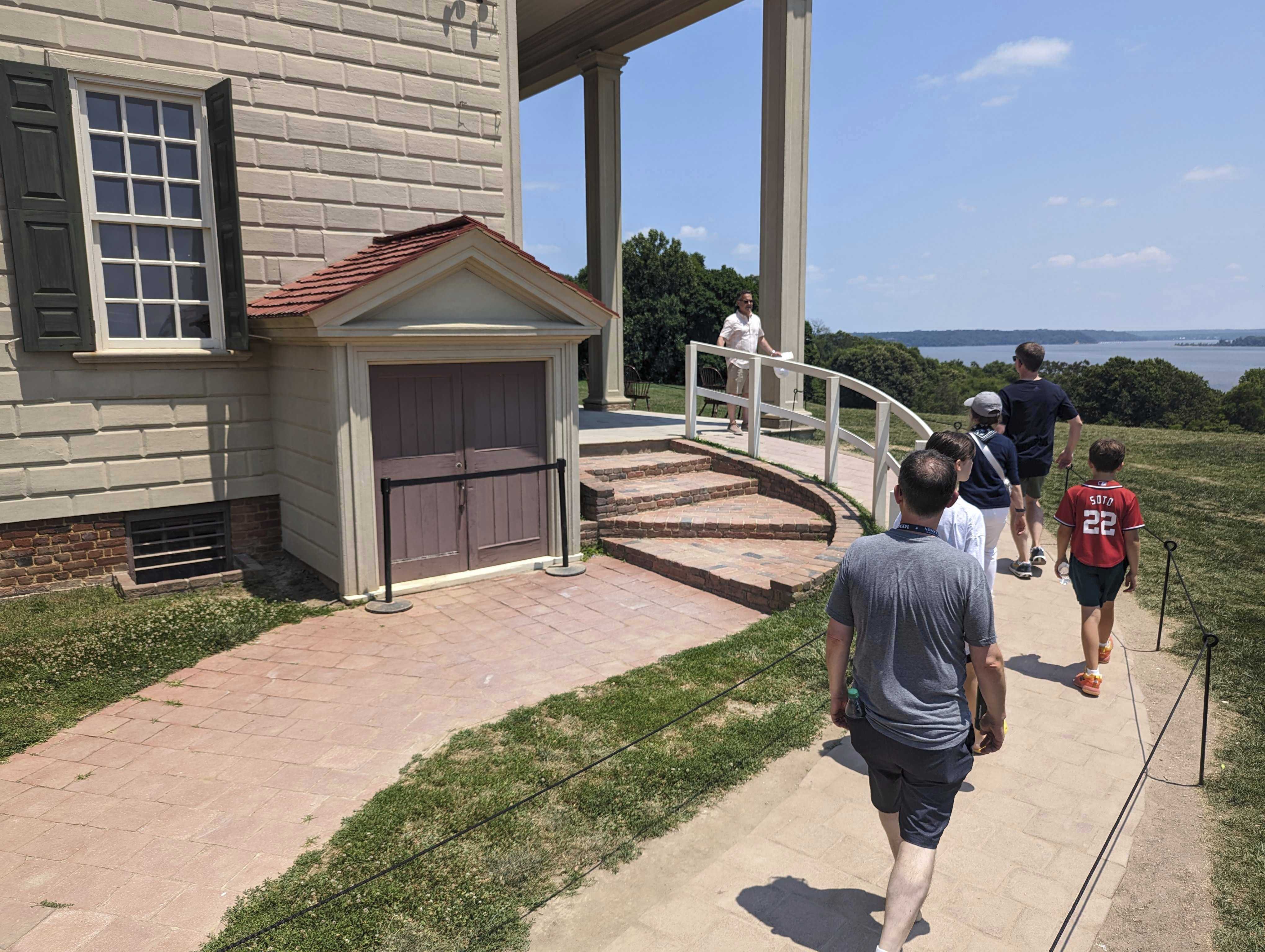 Tourists walk by a cellar door at George Washington's residence in Mount Vernon, Va., Monday, June 17, 2024. Earlier this year archaeologists unearthed a few dozen 18th-century glass bottles containing fruit underneath the Mansion of America's first president. (AP Photo/Nathan Ellgren)
