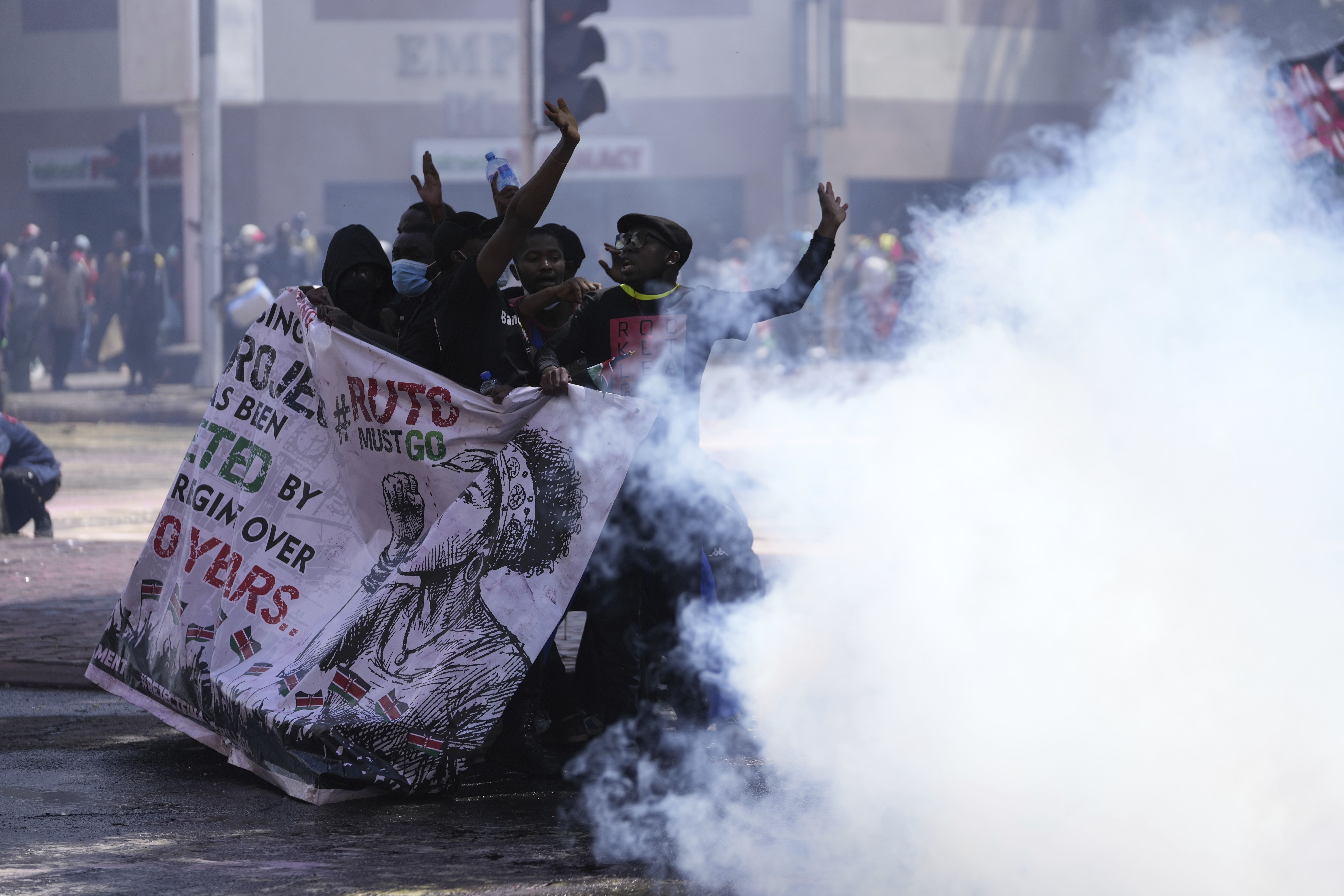 Protesters hide behind a banner as police fire tear gas at them during a protest over proposed tax hikes in a finance bill in downtown Nairobi, Kenya Tuesday, June 25, 2024. (AP Photo/Brian Inganga)
