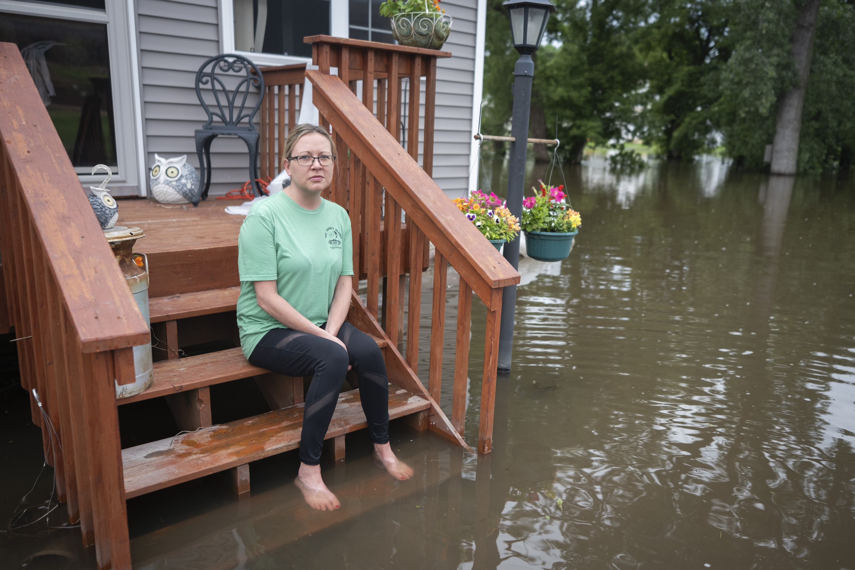 Rachel Morsching sits Tuesday, June 25, 2024, on the flooded porch of her father Dean Roemhildt's home in Waterville., Minn. Waters from the nearby Tetonka and Sakatah lakes have encroached on the town amid recent heavy rains. (Casey Ek/The Free Press via AP)