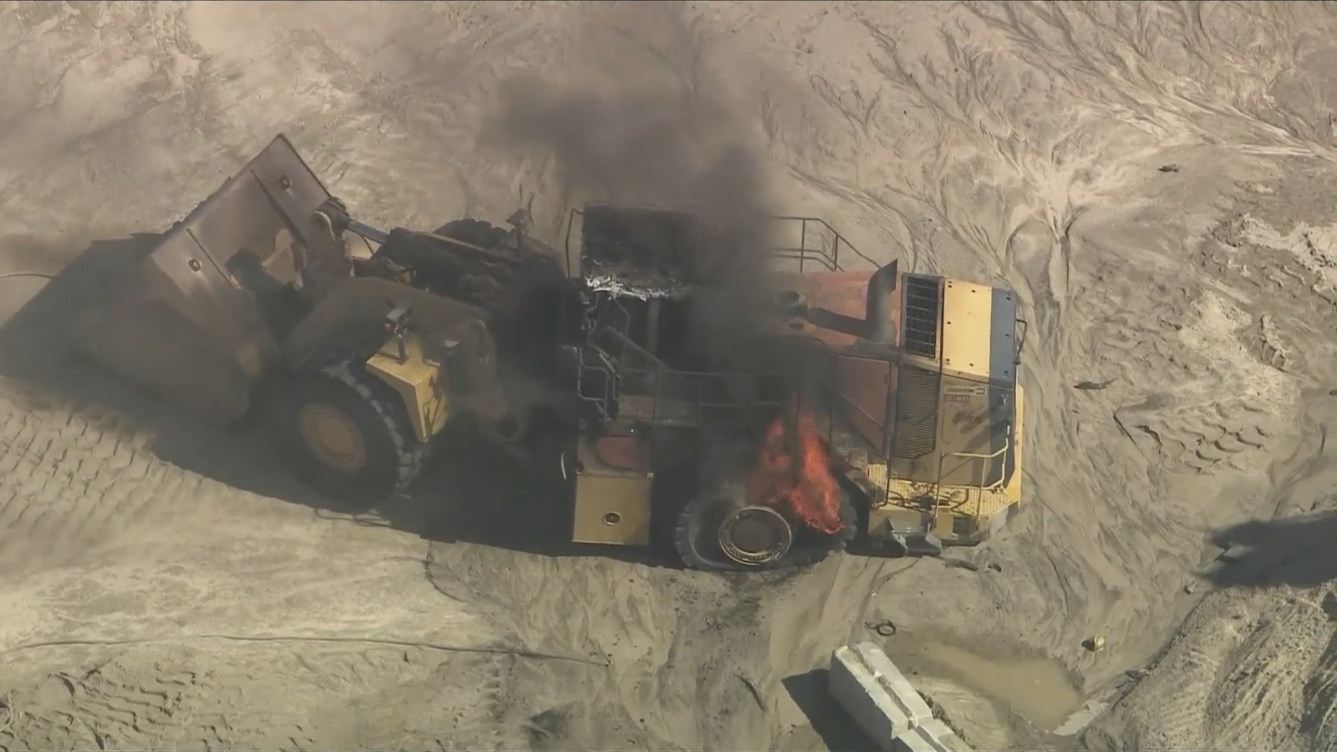 A burning articulated front loader is seen at a quarry after an explosion killed a Los Angeles County firefighter and injured another while they were battling a fire near Palmdale on June 14, 2024. (KTLA)