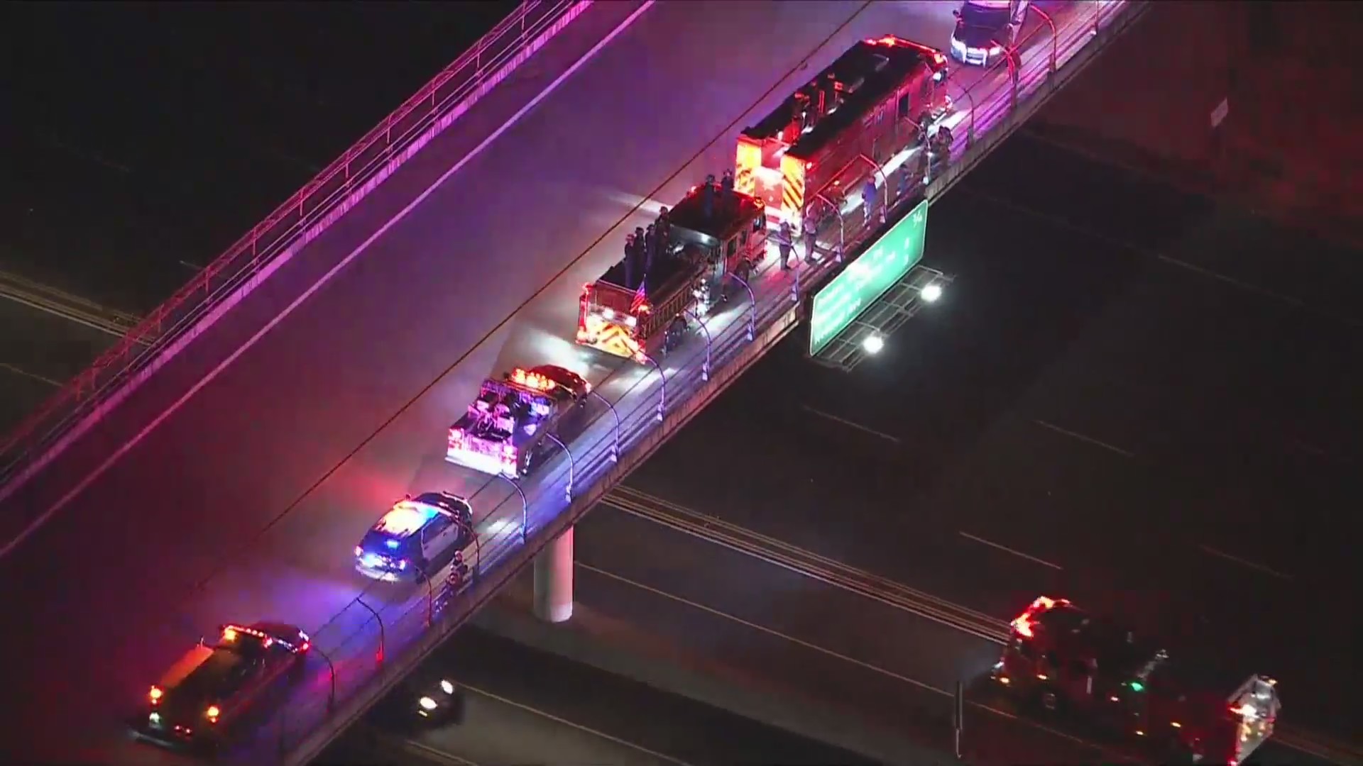 Firefighters and law enforcement saluting Andrew Pontious from a freeway overpass as a procession passes by on June 14, 2024. (KTLA)