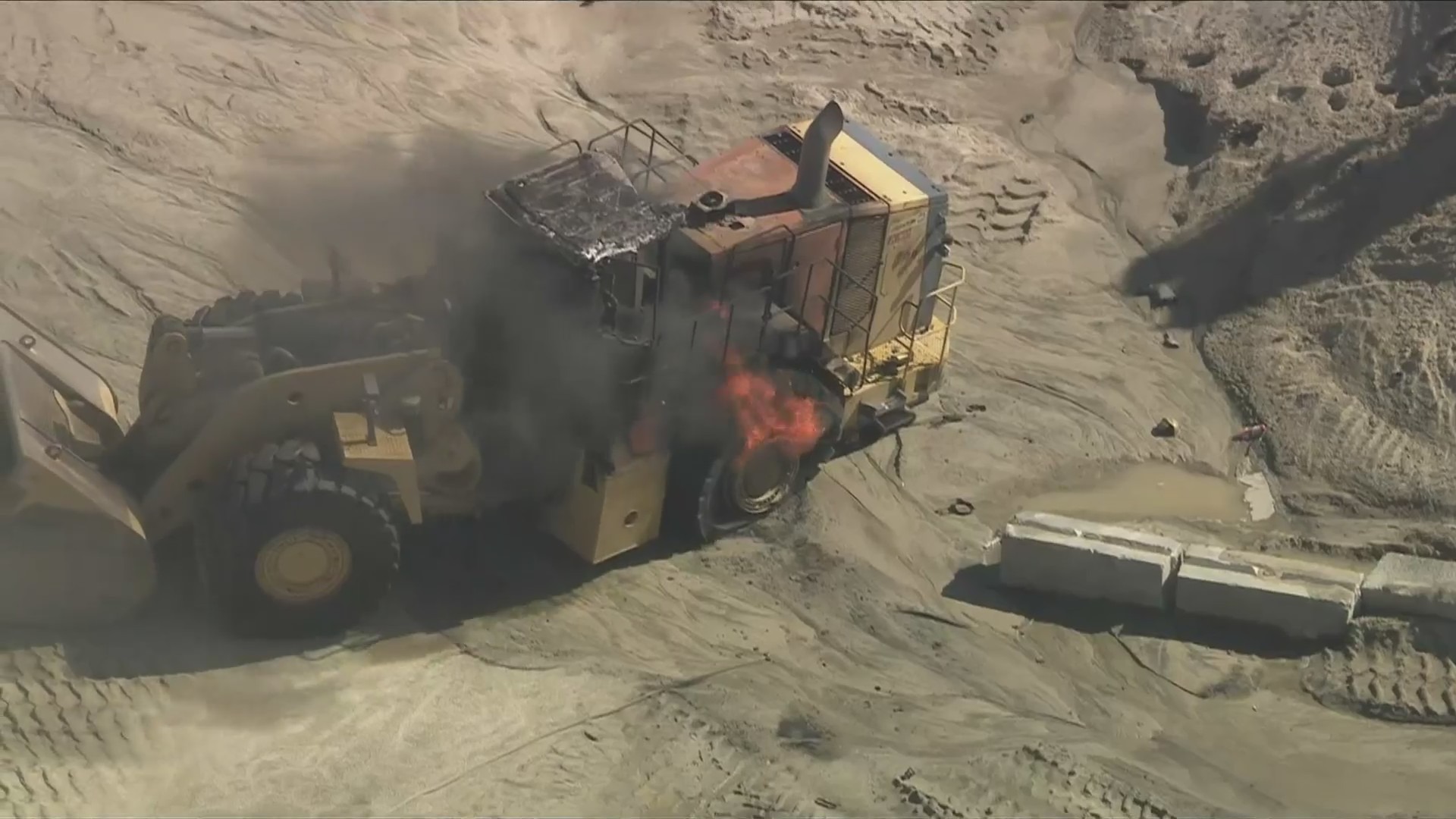 A burning articulated front loader is seen at a quarry after an explosion killed a Los Angeles County firefighter and injured another while they were battling a fire near Palmdale on June 14, 2024. (KTLA)