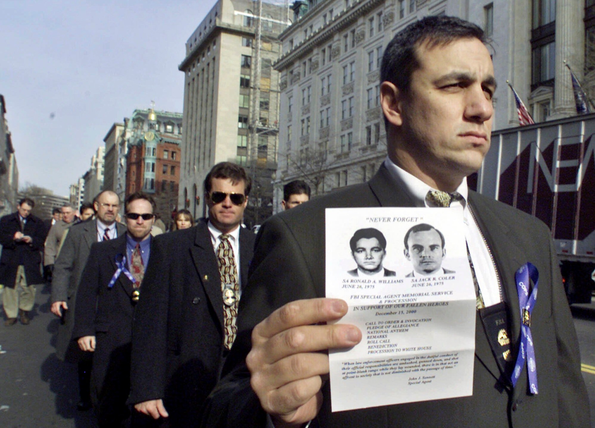 FILE - An unidentified FBI agent, one of the nearly 500 current and retired FBI agents protesting clemency for Leonard Peltier, marches toward the White House, Friday, Dec. 15, 2000, holding an image of two FBI agents, Ron Williams and Jack Coler, who were killed on the Pine Ridge Indian reservation in South Dakota in 1975. Peltier, who has spent most of his life in prison for the killings, has a parole hearing Monday, June 10, 2024, at a federal prison in Florida. (AP Photo/Hillery Smith Garrison, File)