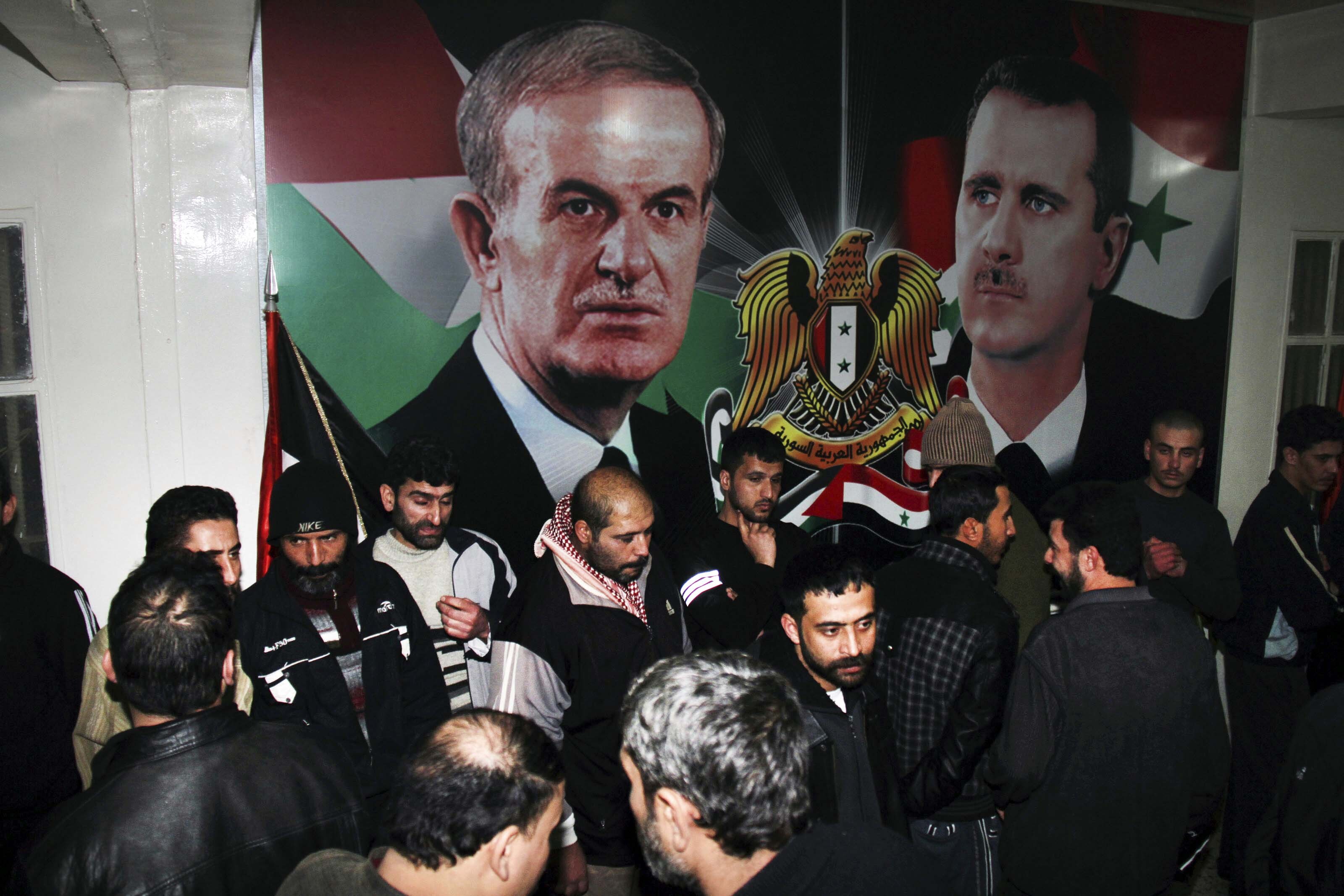 FILE - Freed Syrian detainees gather in front of posters showing Syrian President Bashar Assad, right, and his father Hafez Assad after they were released from Adra Prison on the north-east outskirts of Damascus, Syria, on Jan. 15, 2013. A former Syrian military official who oversaw the prison where human rights officials say torture and abuse took place has been arrested in Los Angeles on suspicion of immigration fraud. (AP Photo/Bassem Tellawi, File)