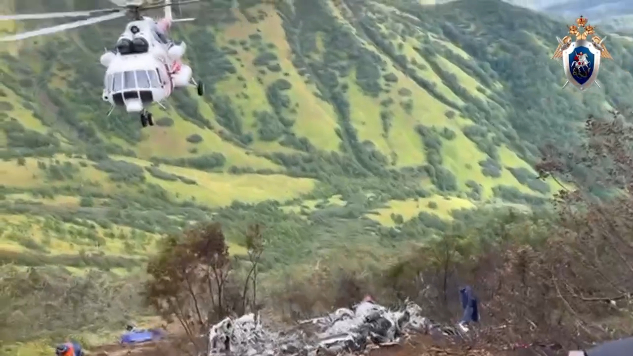 In this photo taken from video released by Investigative Committee of Russia on Monday, Sept. 2, 2024, A Mi-8 helicopter flies over as Russian Investigative Committee employees work at the crash site of the Mi-8 helicopter that was carrying 19 passengers and three crew members on board in Kamchatka region of Russia's Far East. (Investigative Committee of Russia via AP)