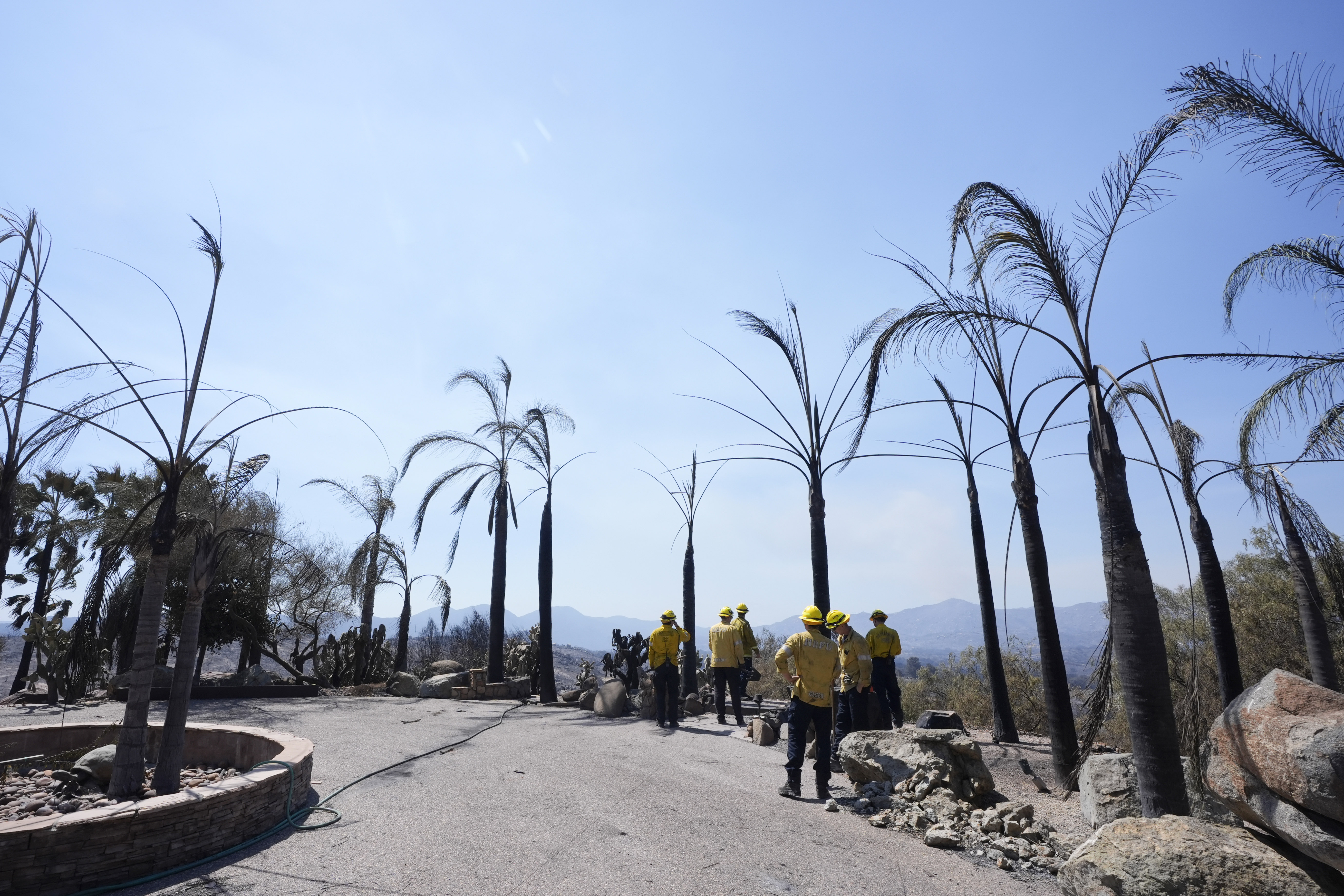 Fire Crews stand on property damaged by the Airport Fire Thursday, Sept. 12, 2024, in El Cariso Village, in unincorporated Riverside County, Calif. (AP Photo/Gregory Bull)