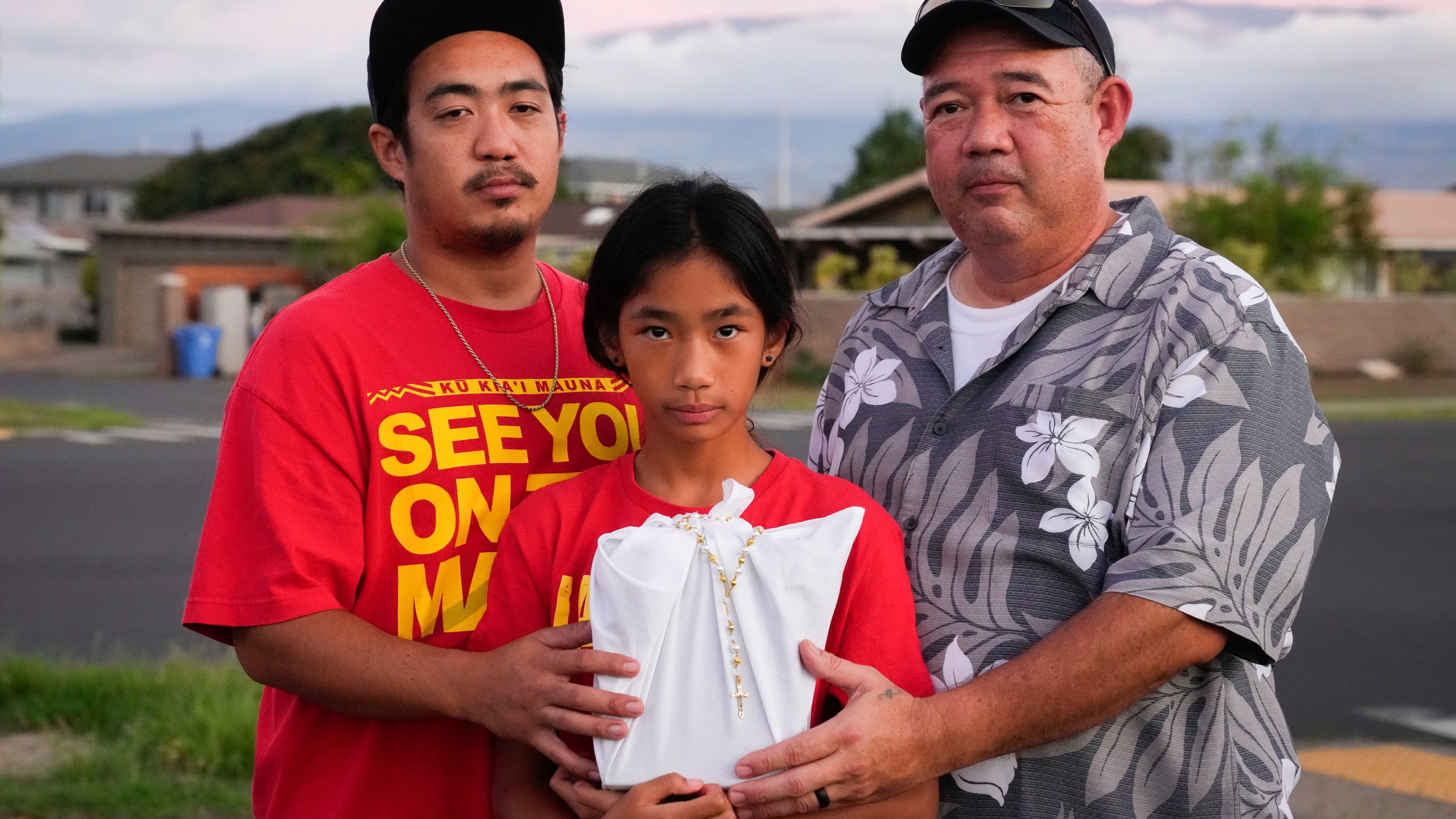 FILE - Briena Mae Rabang, 10, holds the ashes of her great-grandmother Sharlene Rabang, who was named as the 100th victim of the Lahaina wildfire, while posing for a photo with her father Branden, left, and grandfather Brandon, right, Friday, Dec. 8, 2023, in Kahului, Hawaii. (AP Photo/Lindsey Wasson, File)