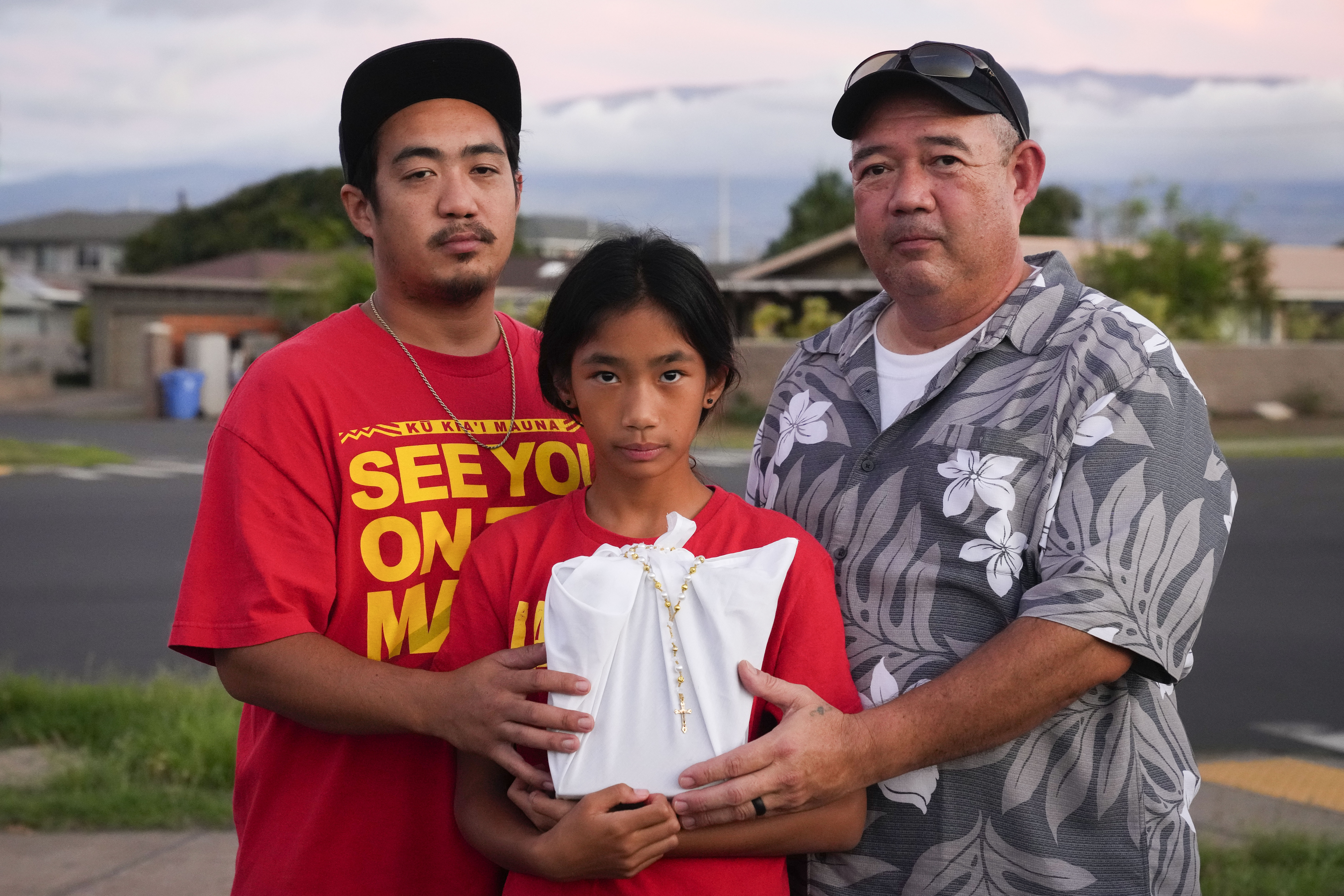 FILE - Briena Mae Rabang, 10, holds the ashes of her great-grandmother Sharlene Rabang, who was named as the 100th victim of the Lahaina wildfire, while posing for a photo with her father Branden, left, and grandfather Brandon, right, Friday, Dec. 8, 2023, in Kahului, Hawaii. (AP Photo/Lindsey Wasson, File)