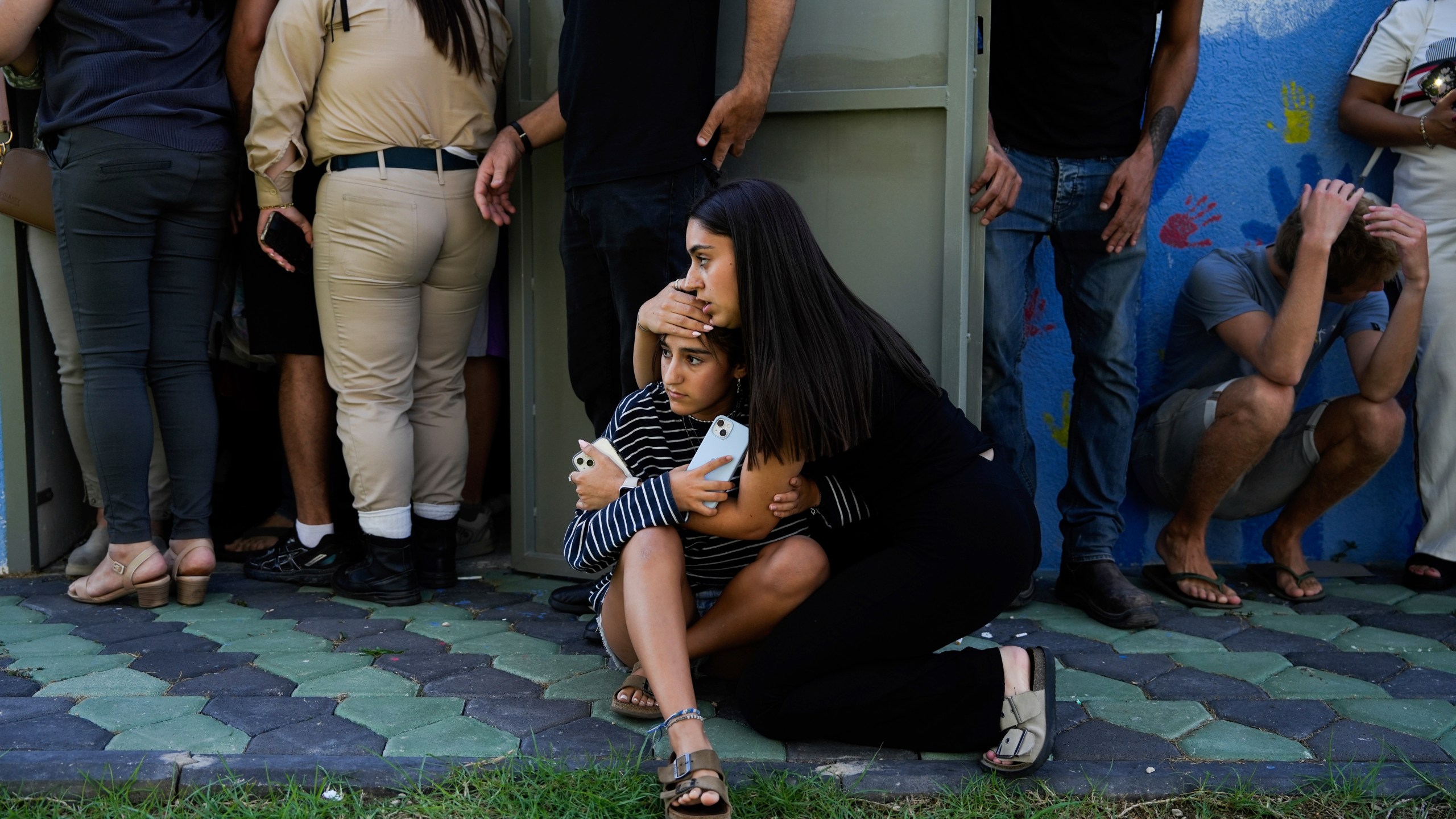 Israelis take cover next to a shelter as a siren sounds a warning of incoming rockets fired from Lebanon, in Nahariya, northern Israel, Thursday, Sept. 19, 2024. (AP Photo/Baz Ratner)