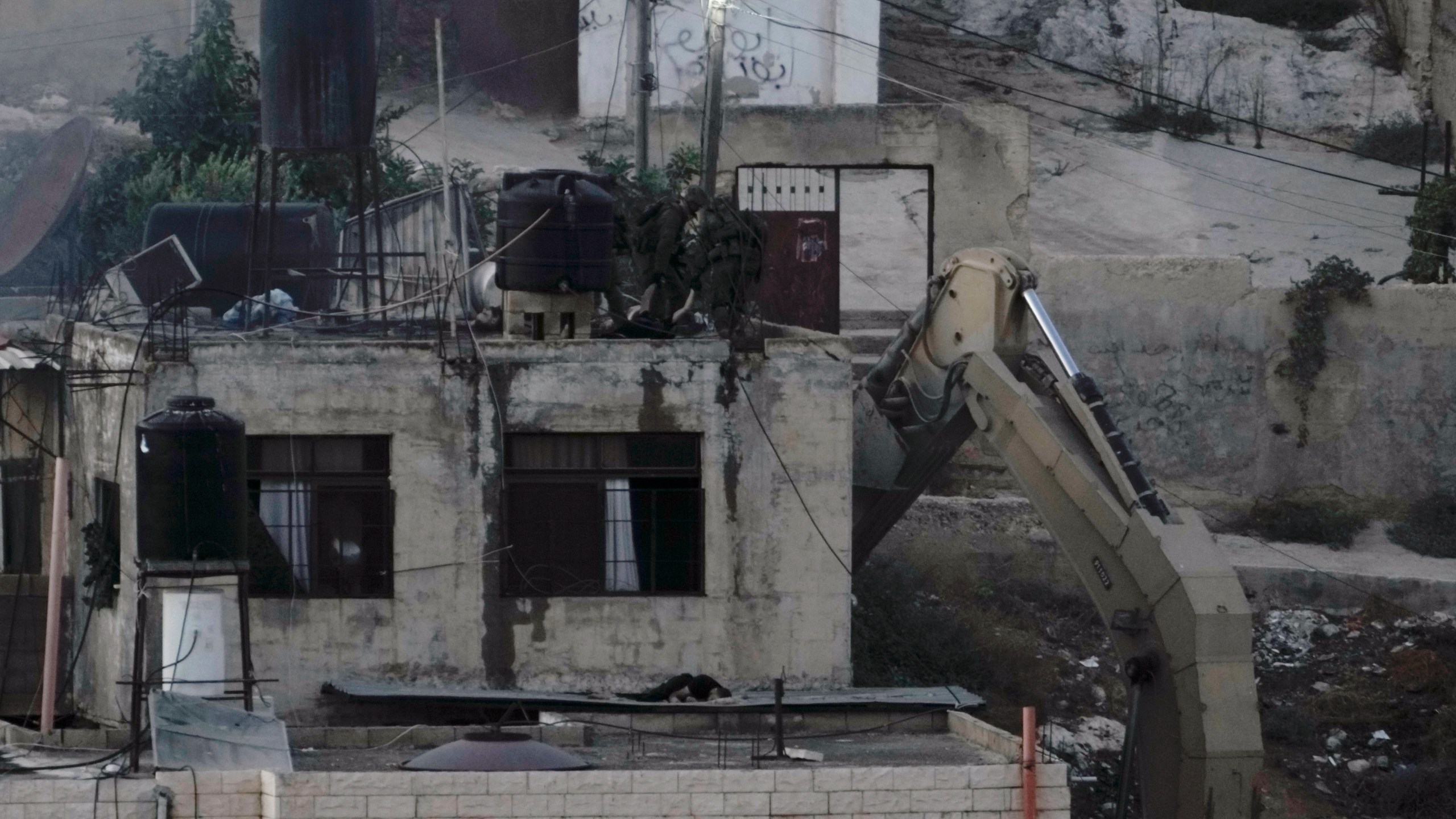 EDS NOTE: GRAPHIC CONTENT - Israeli soldiers look over a rooftop where two lie motionless in the West Bank town of Qabatiya during a raid, Thursday, Sept.19, 2024. (AP Photo/Majdi Mohammed)