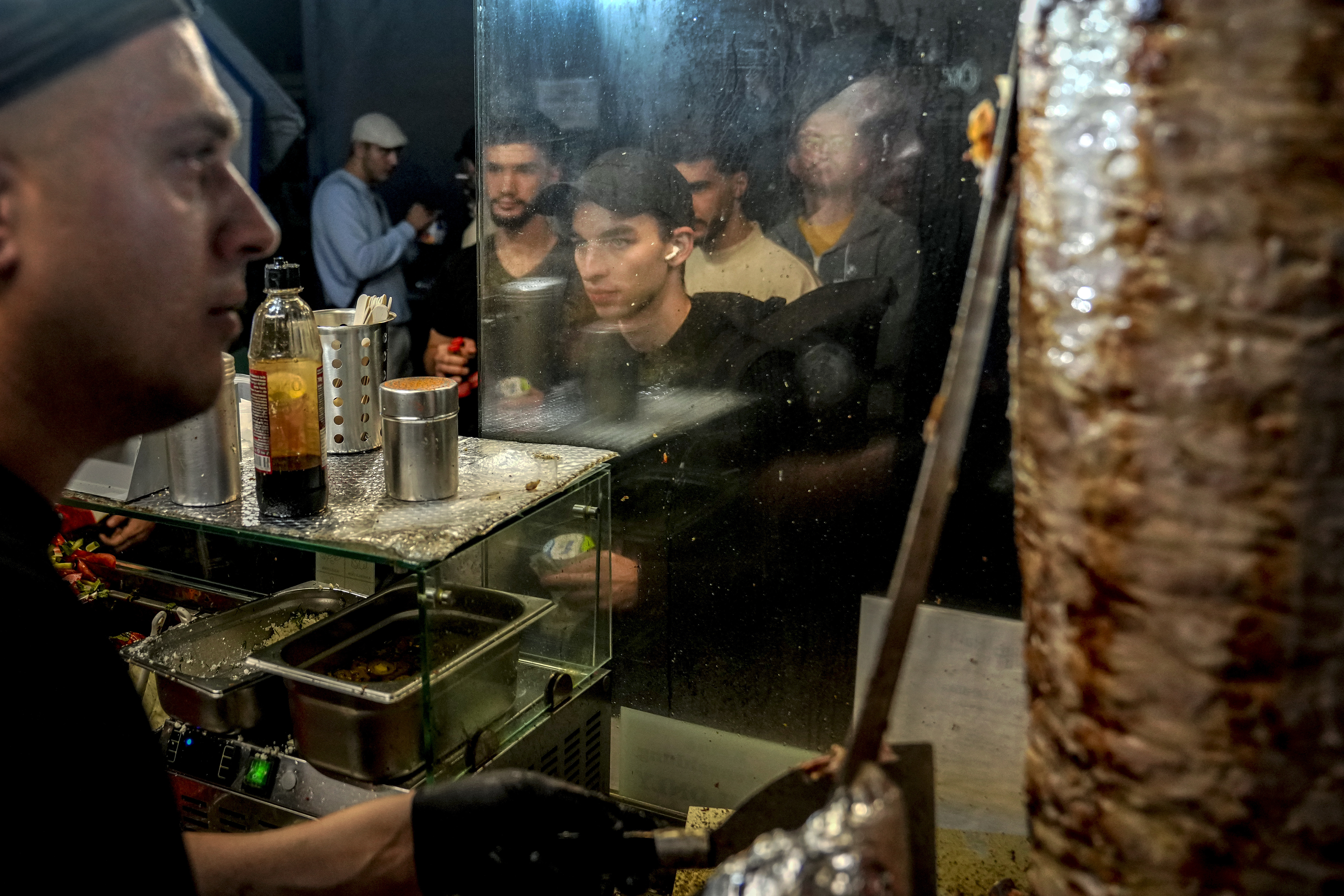 People stand in the line to buy doner kebab while the Turkish cook prepares the doner kebabs, in Berlin, Germany, Wednesday, Sept. 18, 2024. (AP Photo/Ebrahim Noroozi)