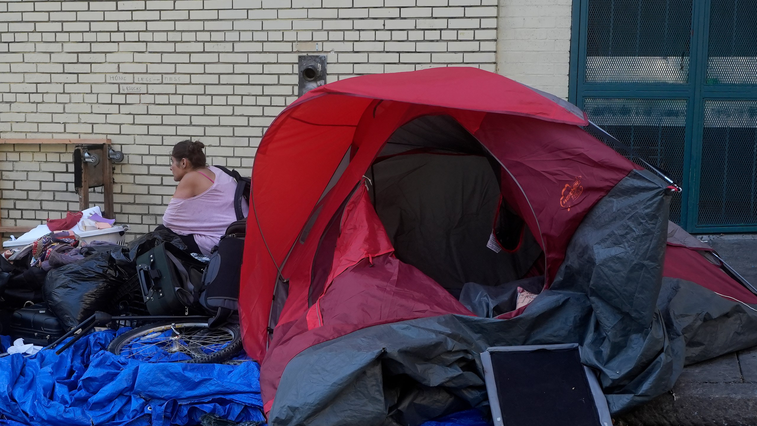 A person sits behind a tent on a sidewalk in San Francisco, Thursday, Aug. 29, 2024. (AP Photo/Jeff Chiu)