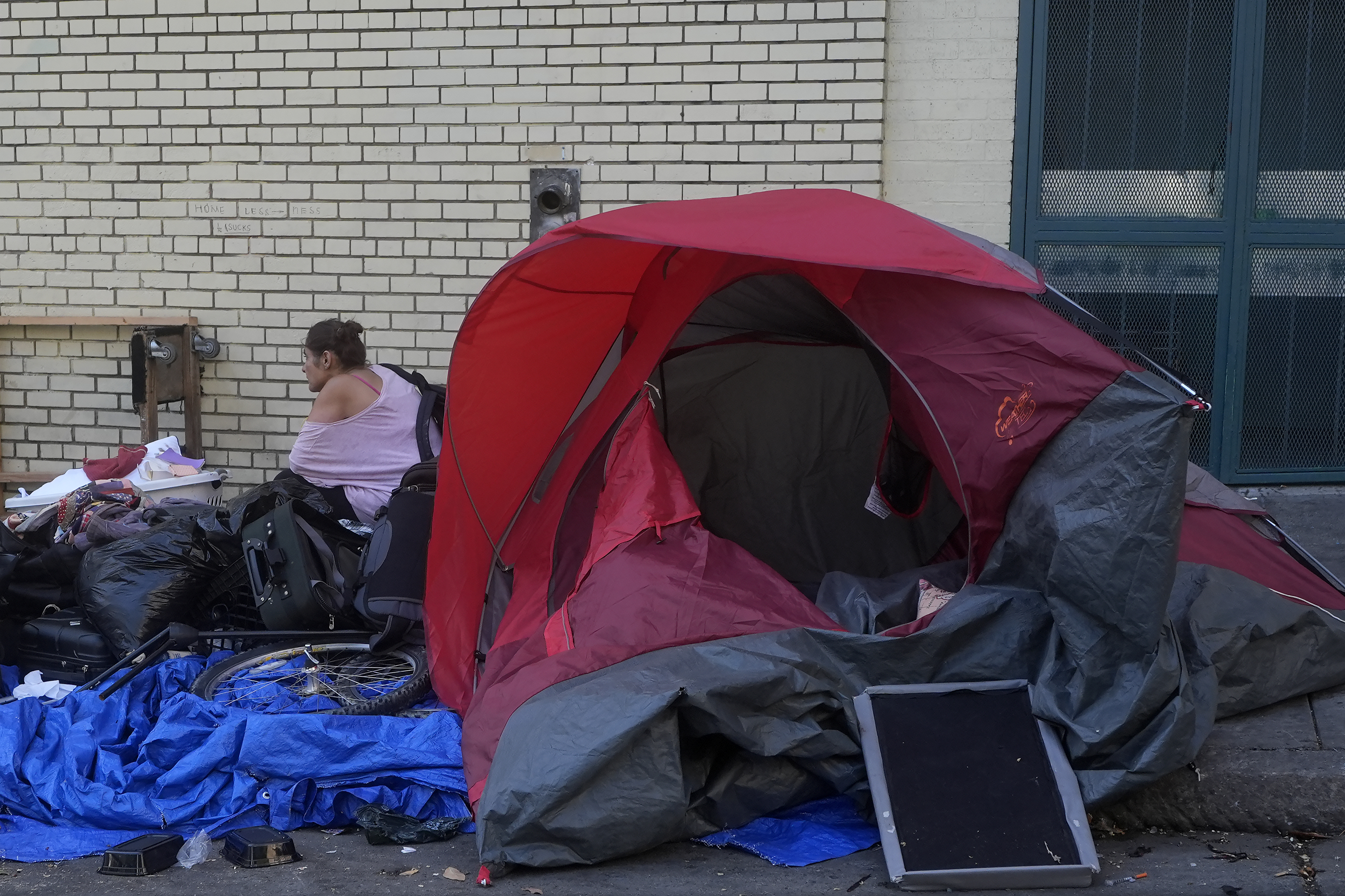 A person sits behind a tent on a sidewalk in San Francisco, Thursday, Aug. 29, 2024. (AP Photo/Jeff Chiu)