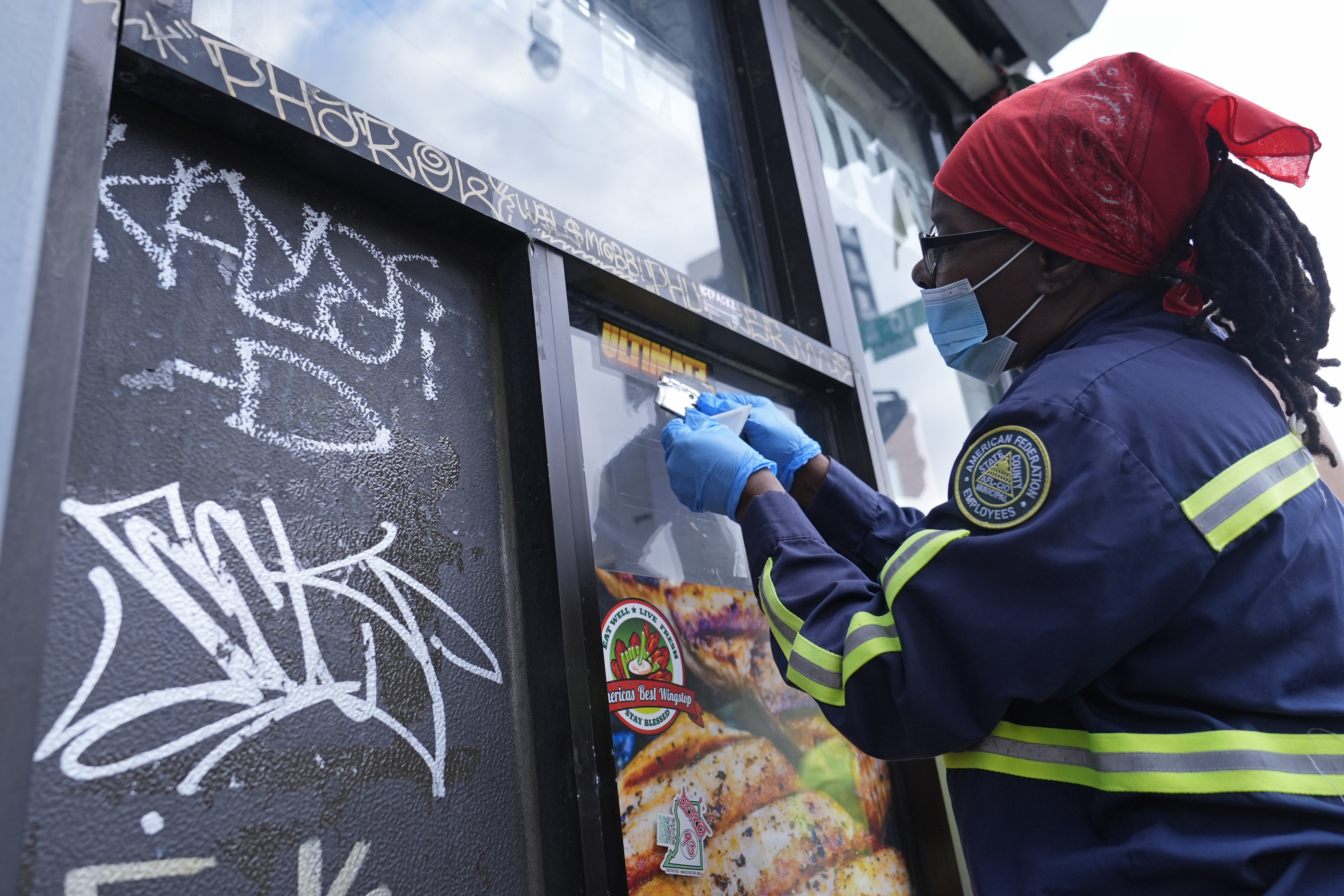 Queen Jones removes a sticker and graffiti in a neighborhood of Washington, Tuesday, Aug. 20, 2024. (AP Photo/Susan Walsh)