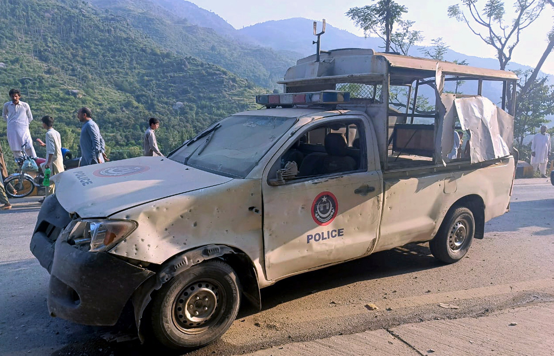 People gather near a damaged police vehicle which was escorting a convoy of foreign diplomats, at the site of a fatal bomb explosion on a road near Malam Jabba, a tourist area in Pakistan's Khyber Pakhtunkhwa province, Sunday, Sept. 22, 2024. (AP Photo/Sherin Zada)