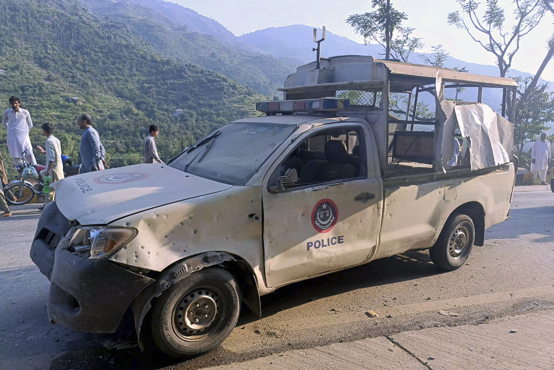 People gather near a damaged police vehicle which was escorting a convoy of foreign diplomats, at the site of a fatal bomb explosion on a road near Malam Jabba, a tourist area in Pakistan's Khyber Pakhtunkhwa province, Sunday, Sept. 22, 2024. (AP Photo/Sherin Zada)