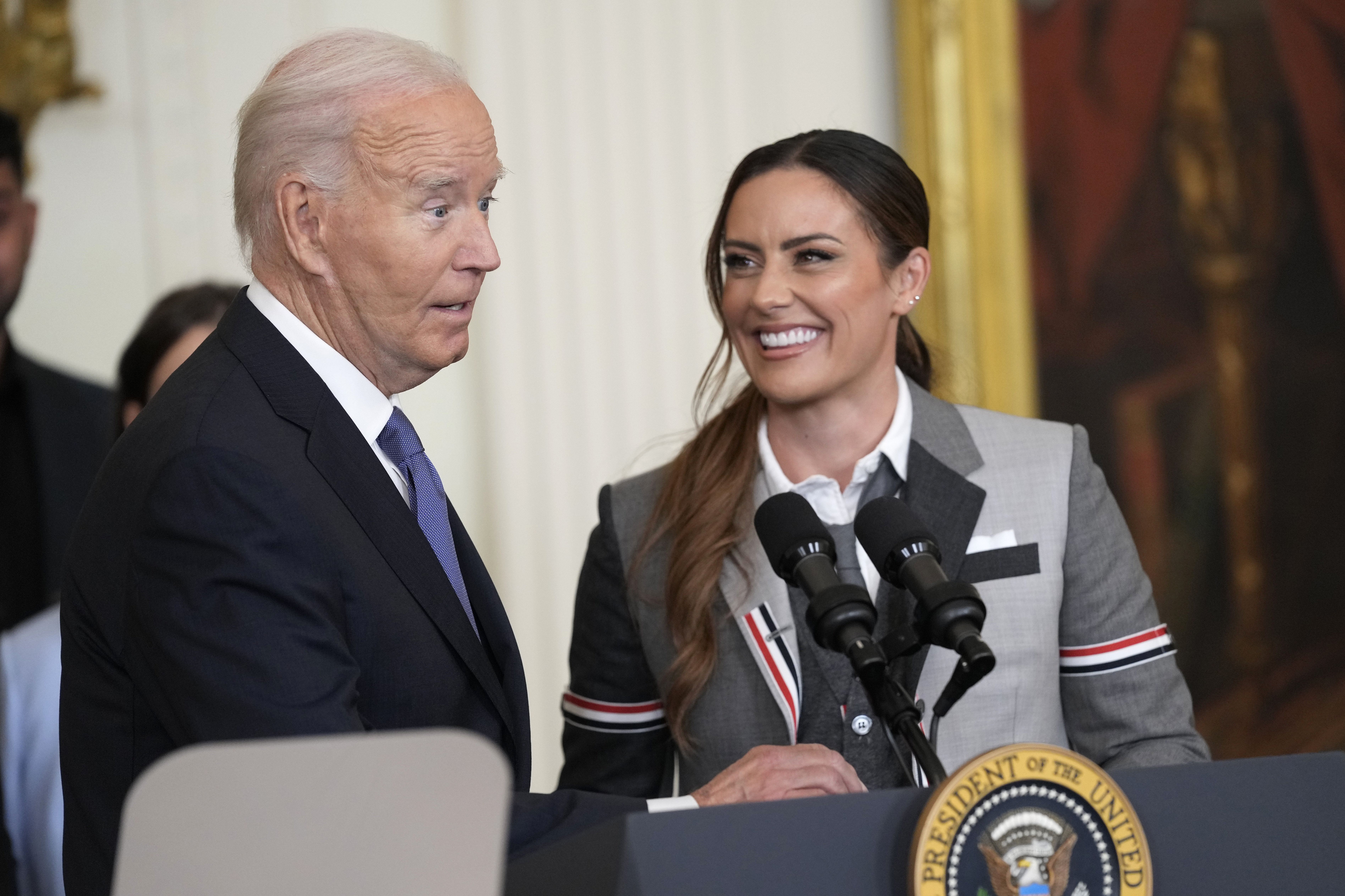 President Joe Biden speaks as Ali Krieger, right, a member of the 2023 NWSL championship NJ/NY Gotham FC team, listens during an event in the East Room of the White House in Washington, Monday, Sept. 23, 2024, to welcome the team and celebrate their championship. (AP Photo/Susan Walsh)