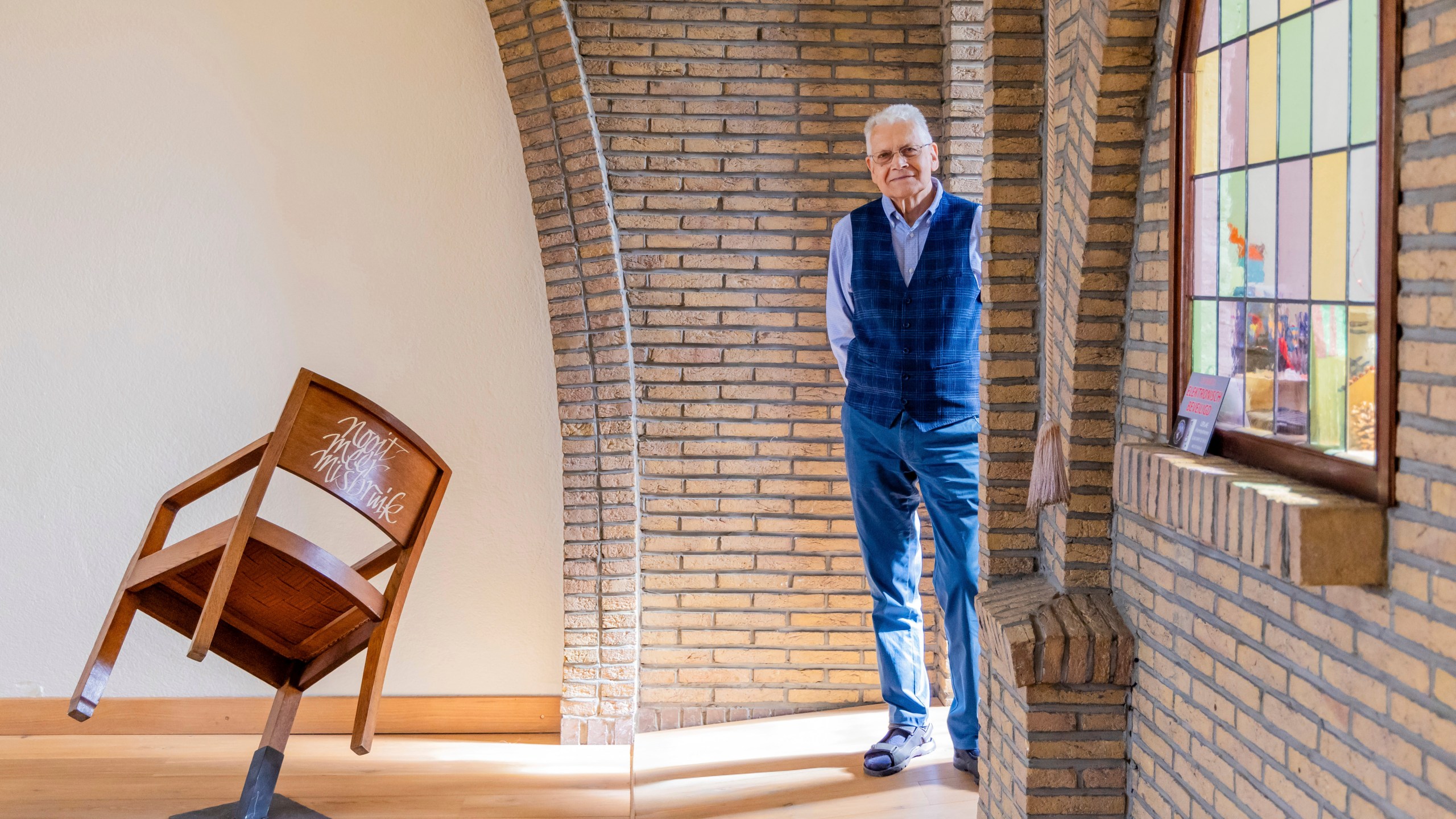 Rik Deville, a retired priest, poses next to a church chair with a message written in Dutch saying "No More Abuse" at the Don Bosco church in Buizingen, Belgium, Sunday, Sept. 8, 2024. (AP Photo/Geert Vanden Wijngaert)