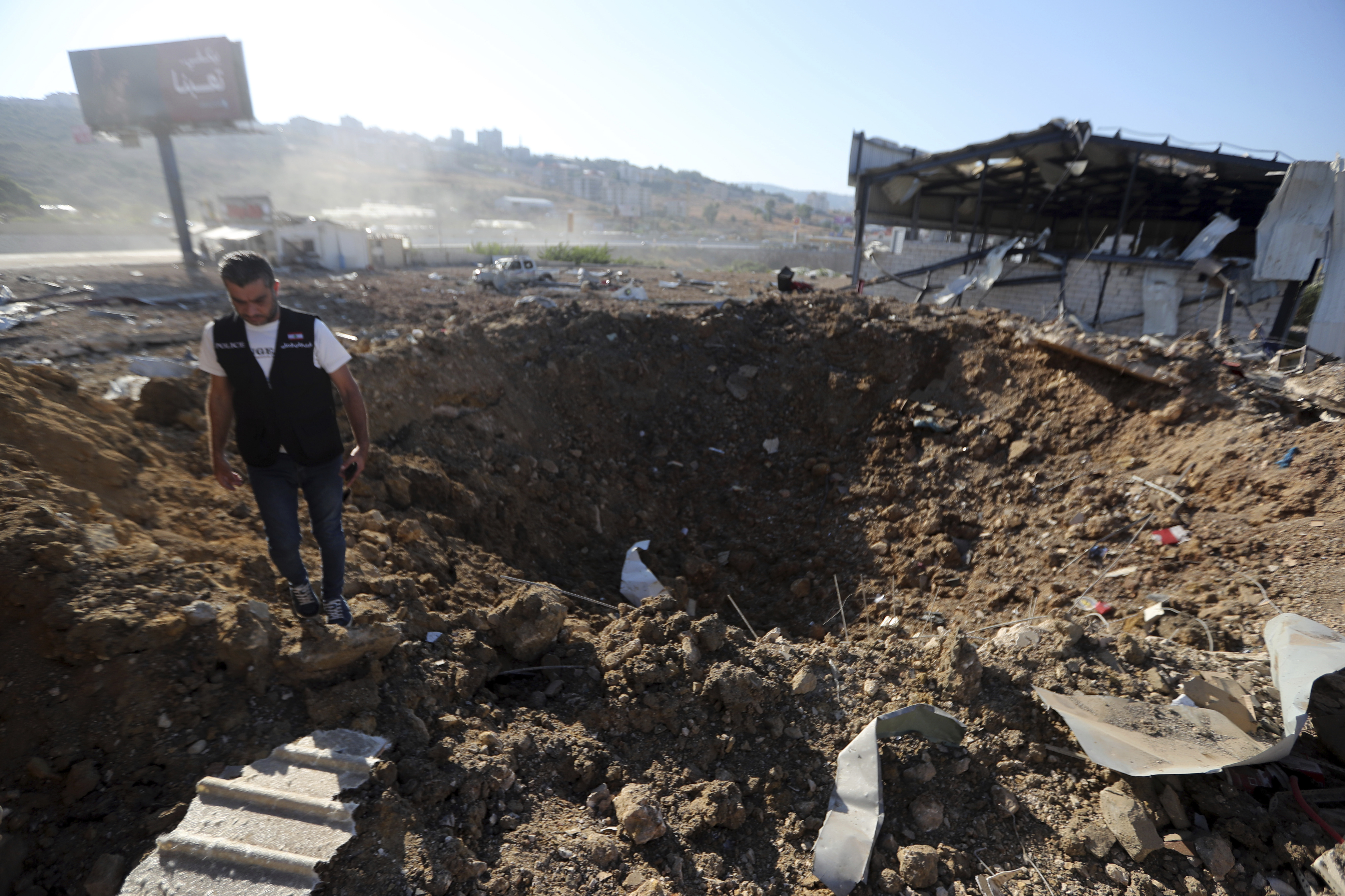 A Lebanese police intelligence stands near a crater at the site of an Israeli airstrike that hit a hangar in the southern town of Jiyeh, Lebanon, Wednesday, Sept. 25, 2024. (AP Photo/Mohammed Zaatari)