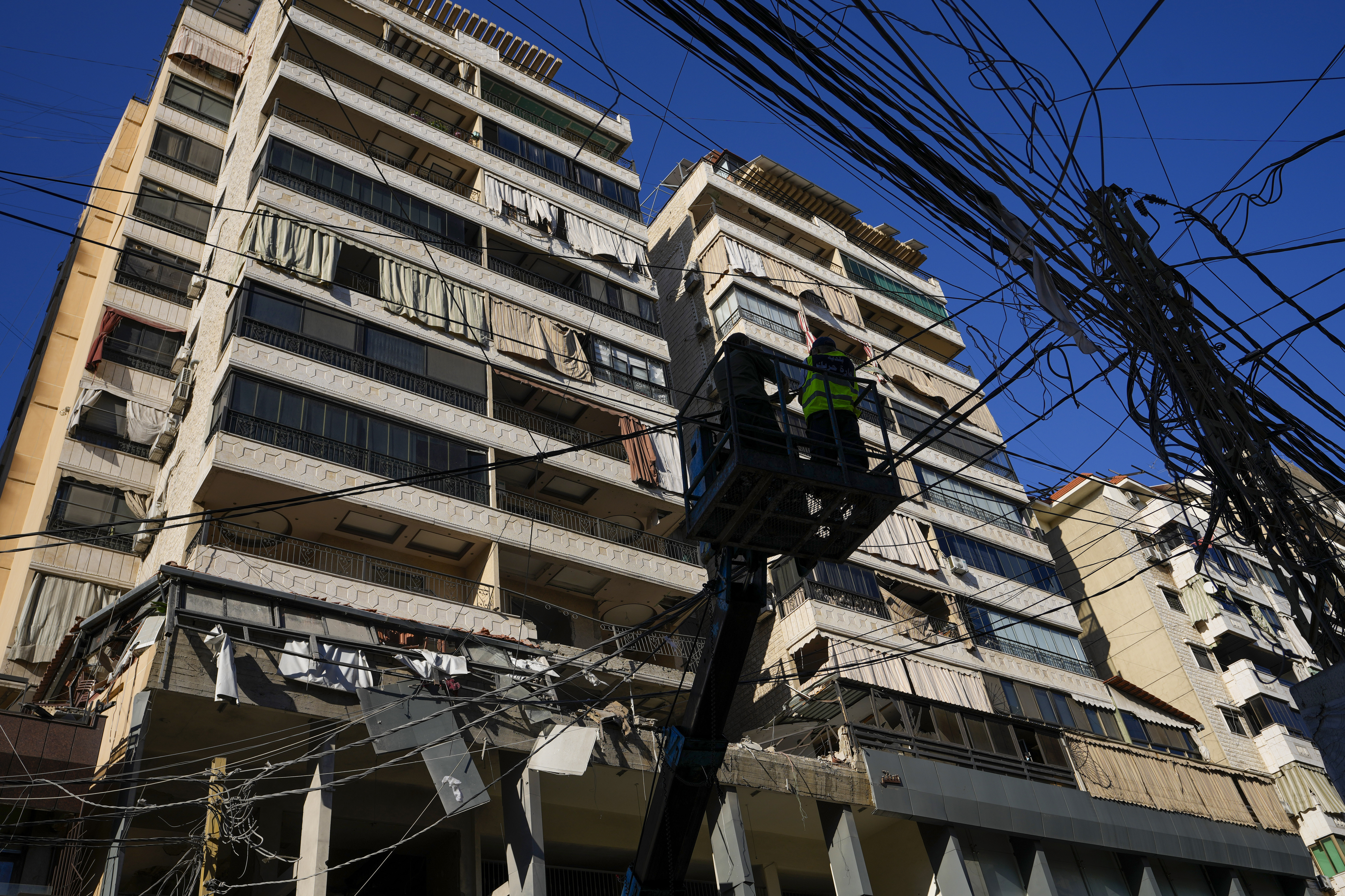 Municipality workers remove power cables in front of damaged buildings at the site of an Israeli airstrike in Beirut's southern suburb, Thursday, Sept. 26, 2024. (AP Photo/Hassan Ammar)