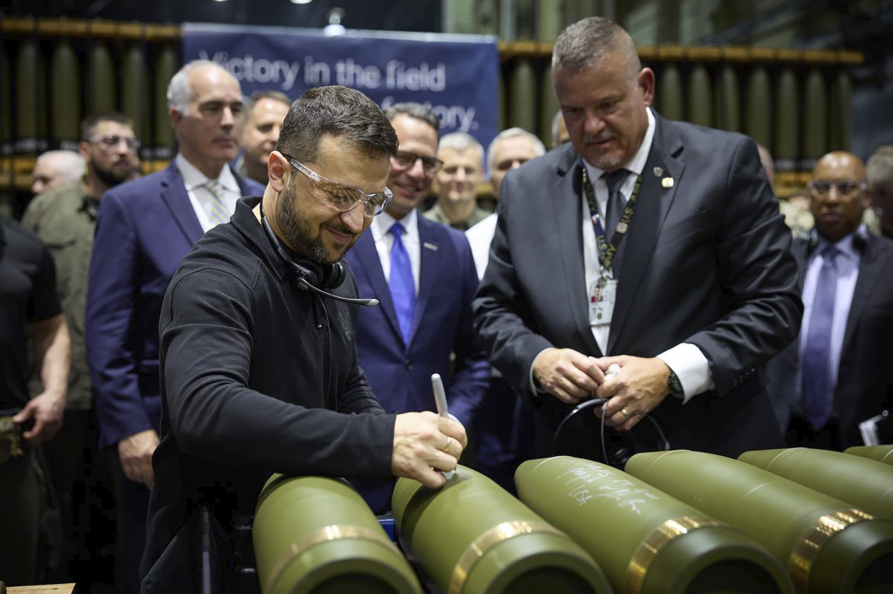 In this image provided by the Office of the Ukrainian Presidency, Ukrainian President Volodymyr Zelenskyy, left, is watched by Rich Hansen, the commander's representative for the Scranton Army Ammunition Plant, while signing military ordnance in Scranton, Pa., Sunday, Sept. 22, 2024. (Office of the Ukrainian Presidency via AP)