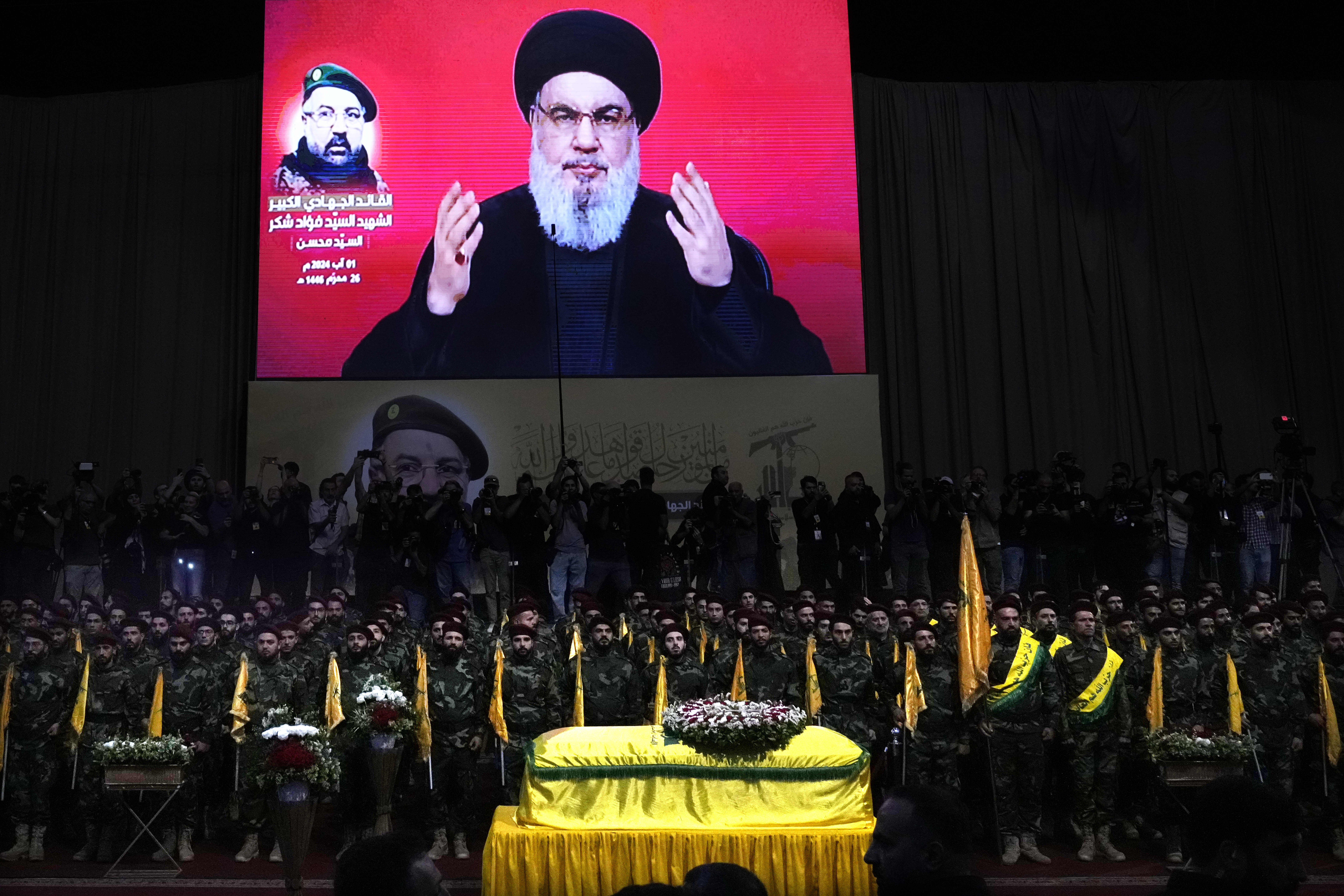 FILE - Hezbollah fighters stand behind the coffin of their top commander Fouad Shukur, who was killed by an Israeli airstrike on July 30, as Hezbollah leader Sayyed Hassan Nasrallah speaks through a screen during Shukur's funeral in a southern suburb of Beirut, Lebanon, Aug. 1, 2024. (AP Photo/Hussein Malla, File)