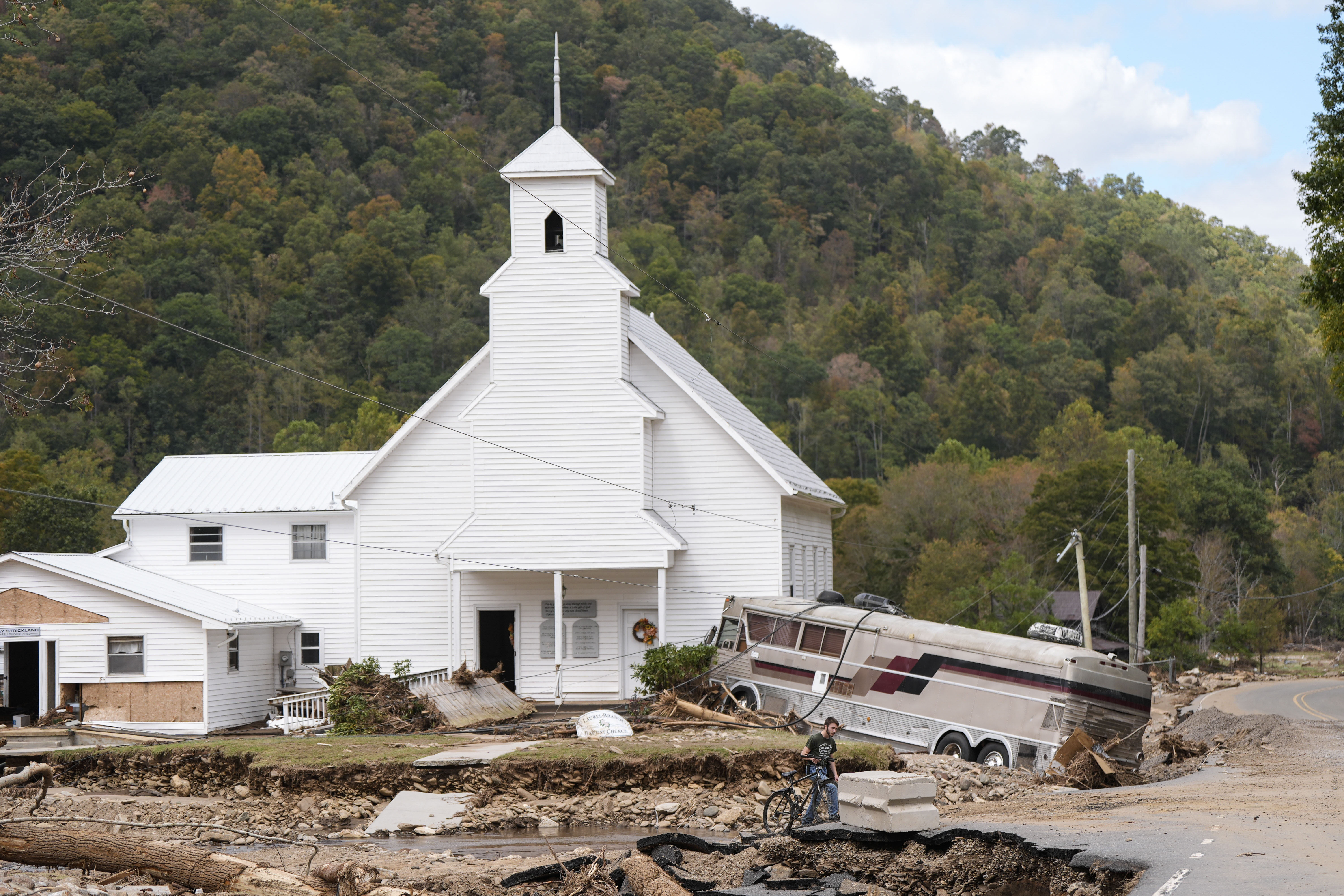 Dominick Gucciardo walks to his home past a bus pushed by flood waters rests against Laurel Branch Baptist church in the aftermath of Hurricane Helene, Thursday, Oct. 3, 2024, in Pensacola, N.C. (AP Photo/Mike Stewart)