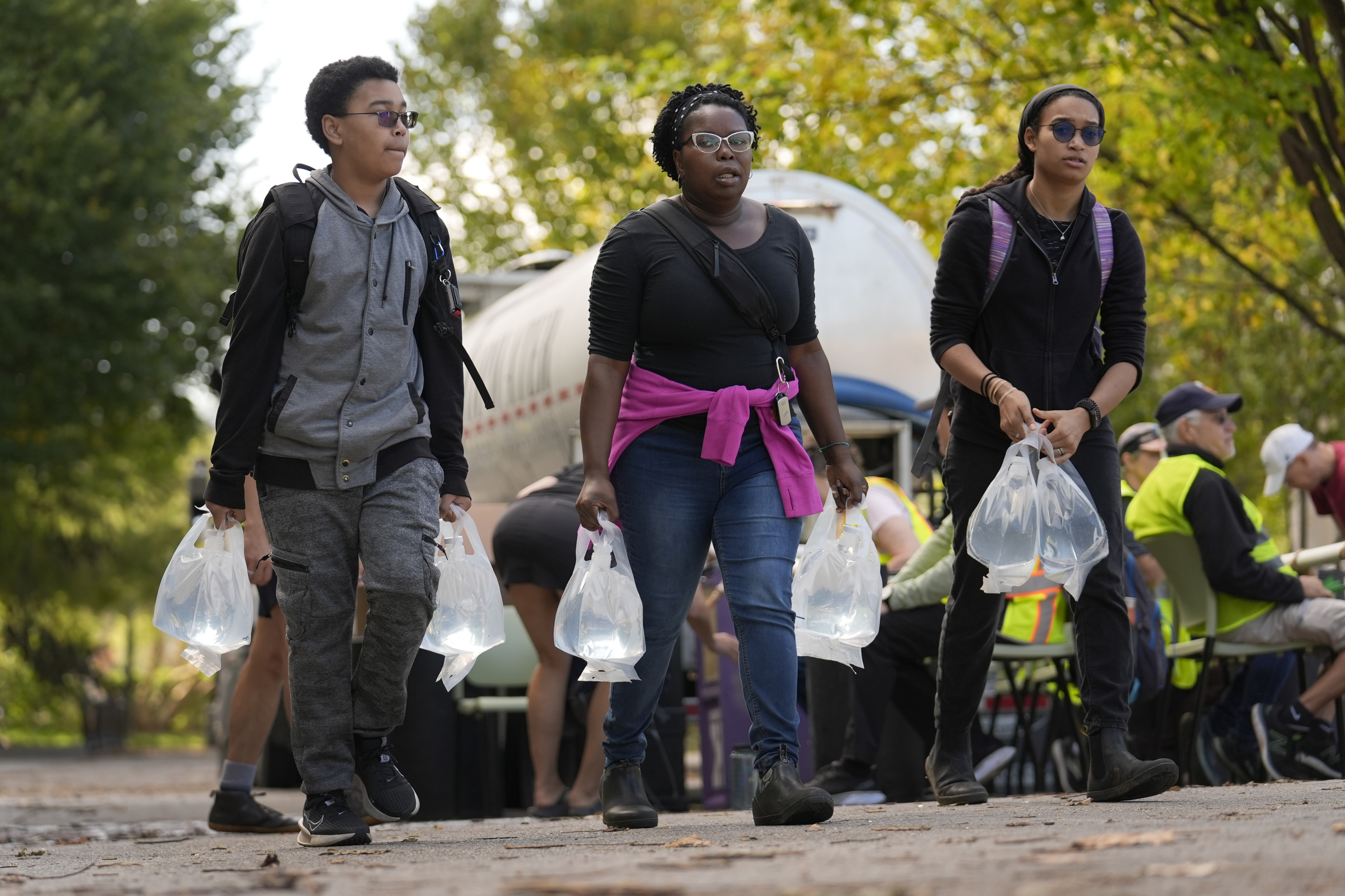 People carry bags of fresh water after filling up at a distribution site in the aftermath of Hurricane Helene Wednesday, Oct. 2, 2024, in Asheville, N.C. (AP Photo/Jeff Roberson)