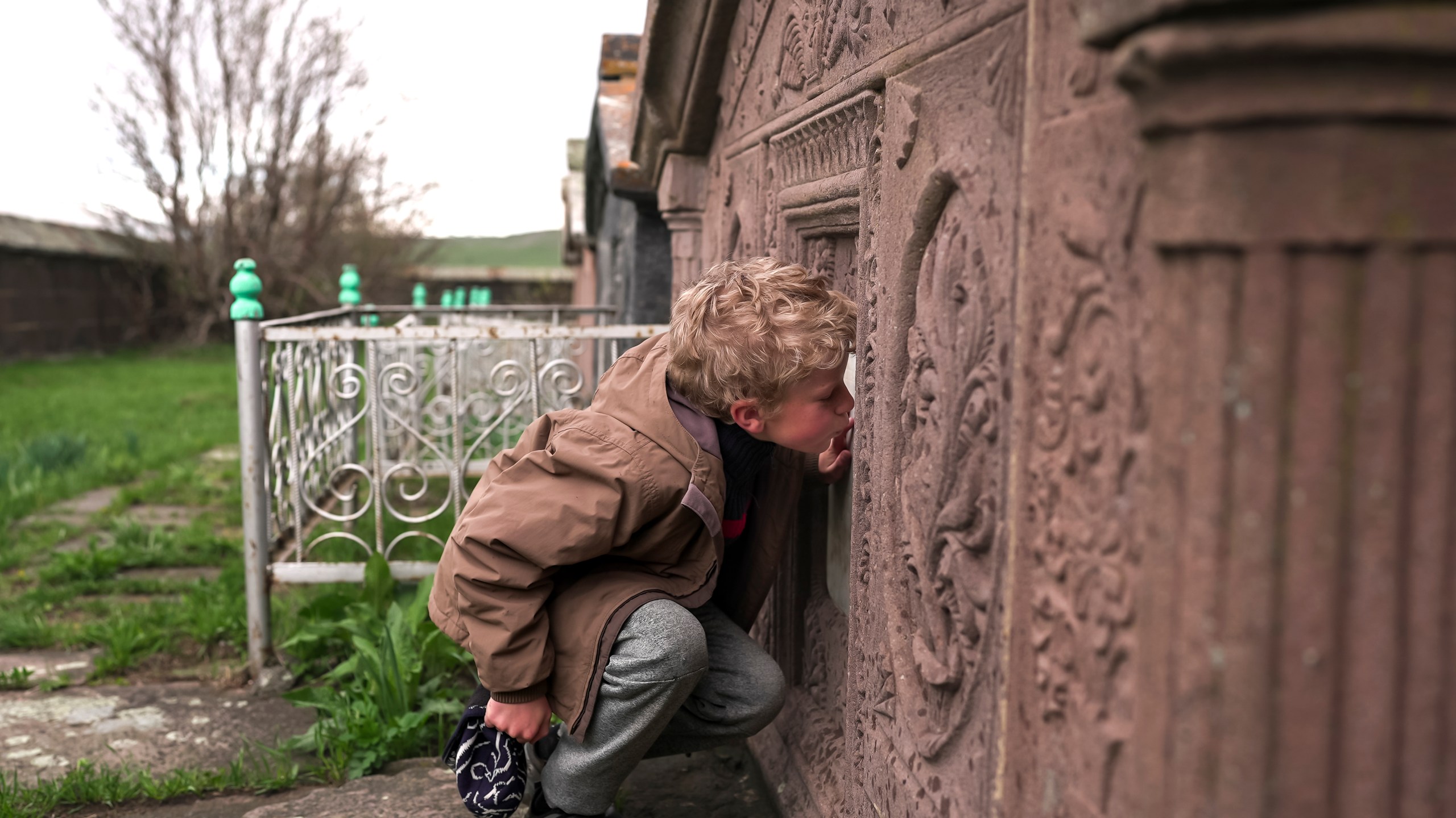 Ilya Strukov, 10, kisses a tombstone on a grave of his Doukhobor ancestors at a cemetery outside of the remote mountain village of Orlovka, Georgia, Sunday, May 5, 2024. (AP Photo/Kostya Manenkov)