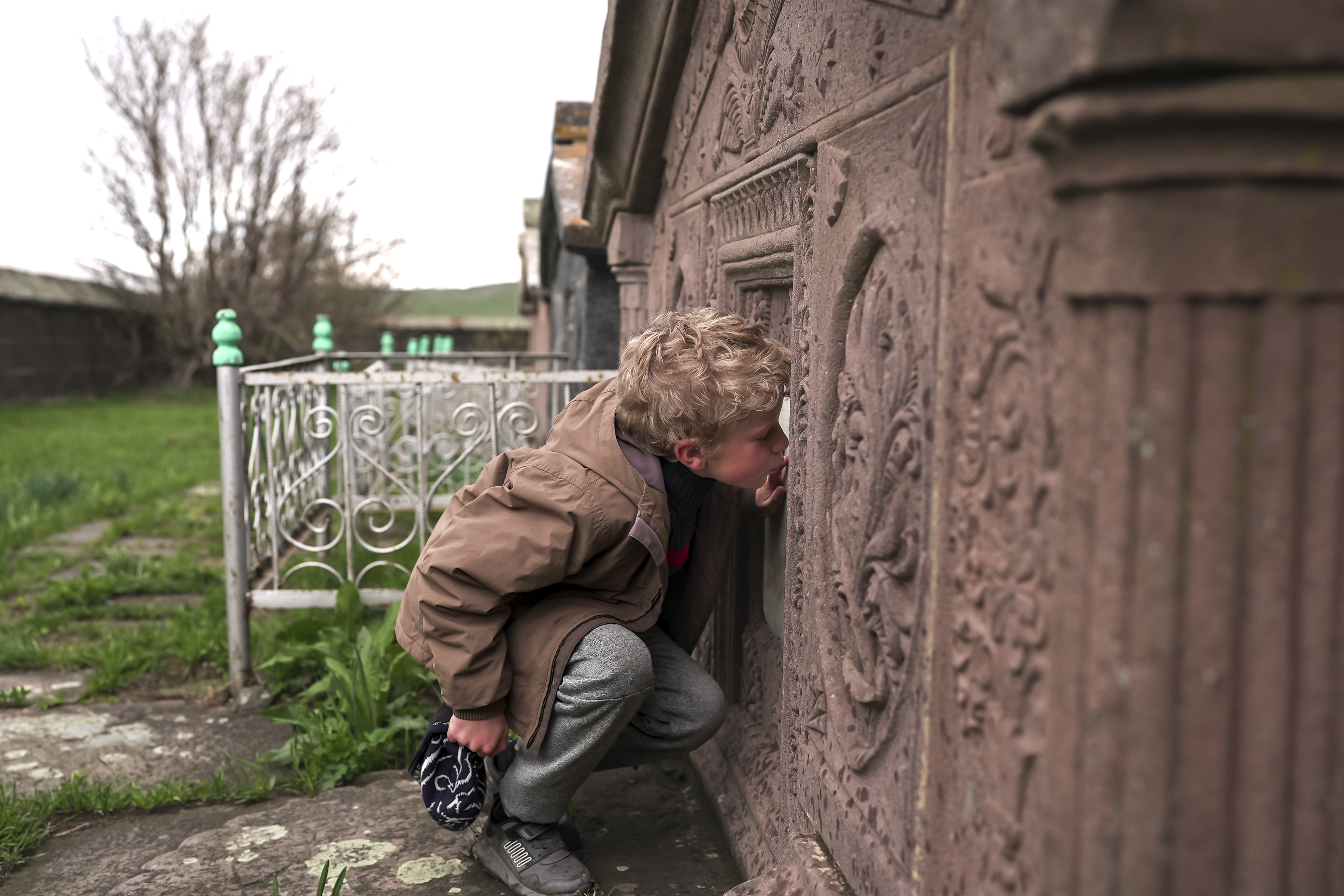 Ilya Strukov, 10, kisses a tombstone on a grave of his Doukhobor ancestors at a cemetery outside of the remote mountain village of Orlovka, Georgia, Sunday, May 5, 2024. (AP Photo/Kostya Manenkov)