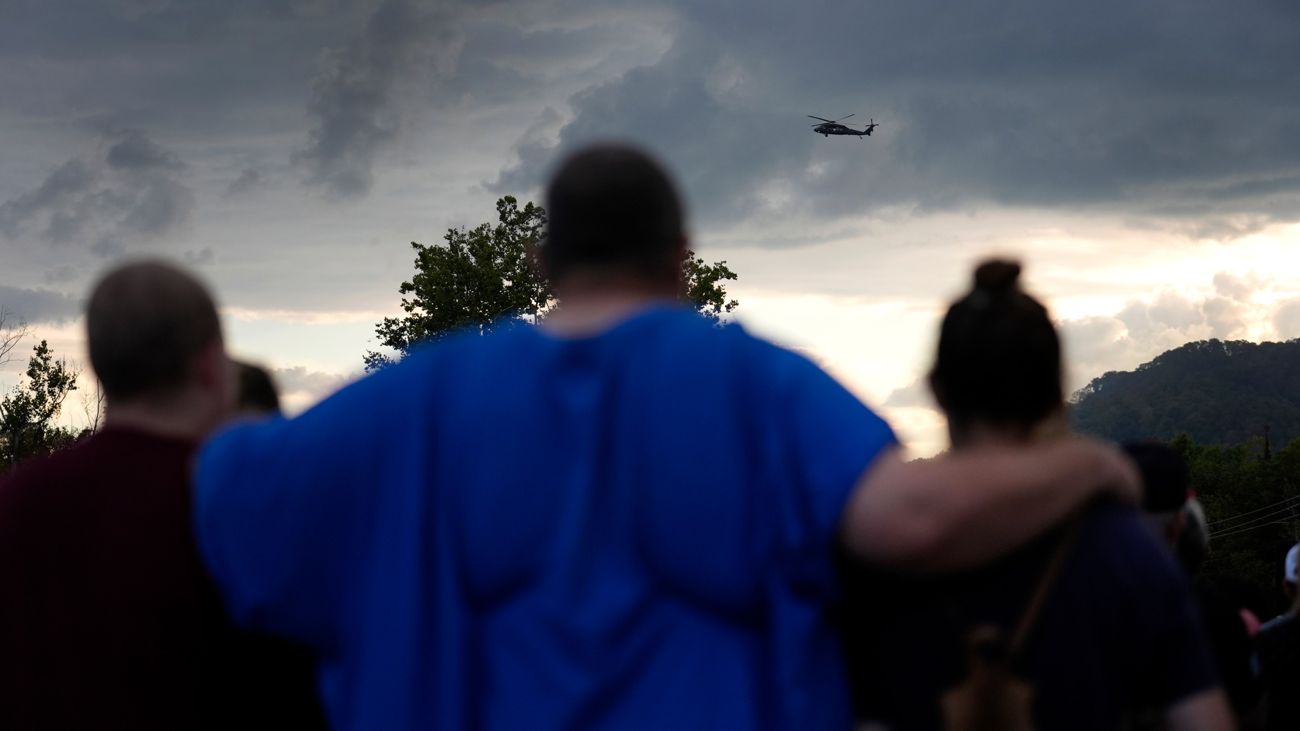 Mourners gather during a vigil for victims of the Impact Plastics tragedy as a helicopter continues search and rescue work over the disaster site in the distance in the days after Hurricane Helene in Erwin, Tenn., on Thursday, Oct. 3, 2024. (AP Photo/Jeff Roberson)