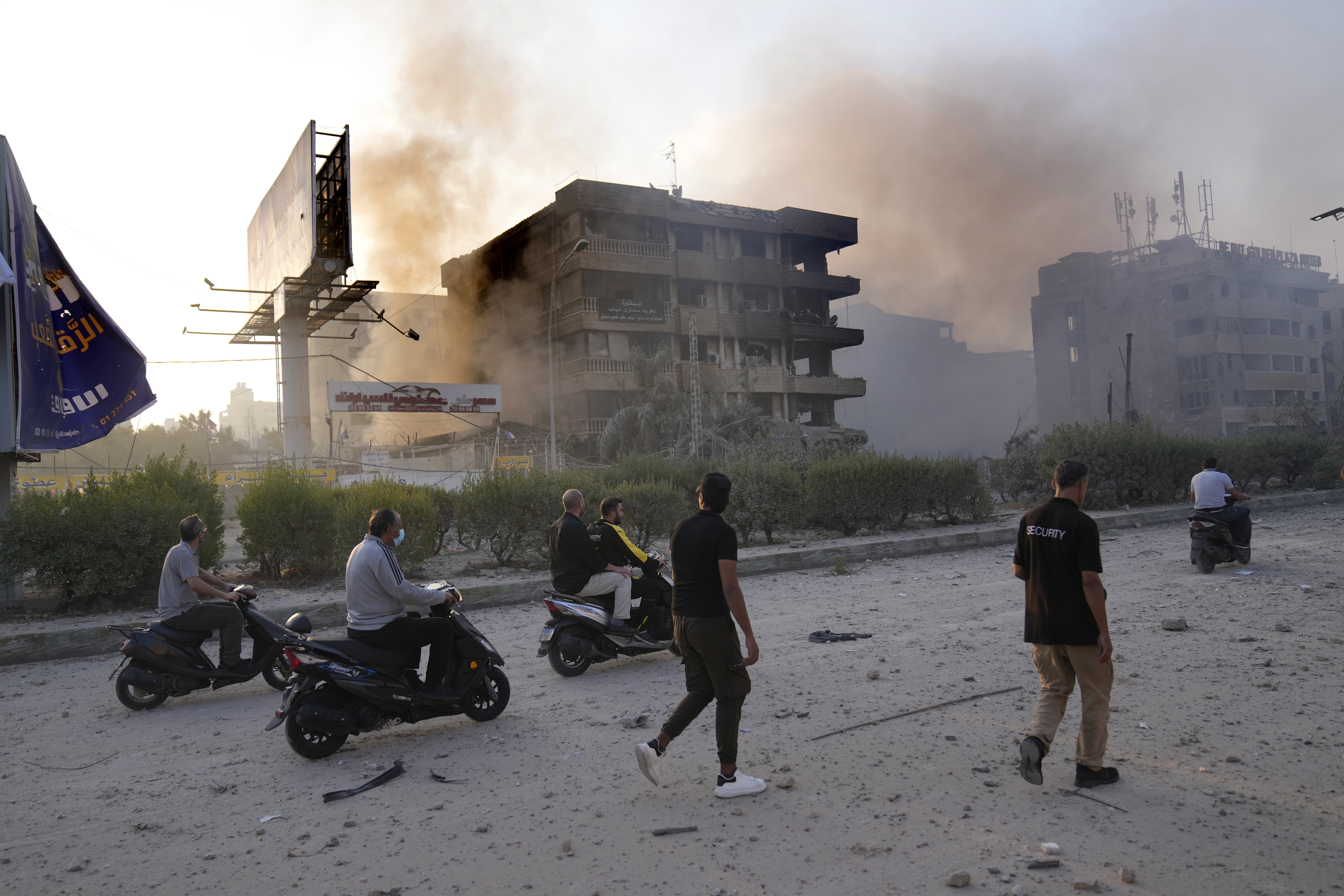 People pass in front of destroyed buildings that were hit by Israeli airstrikes in Dahiyeh, Beirut, Lebanon, Sunday, Oct. 6, 2024. (AP Photo/Hussein Malla)