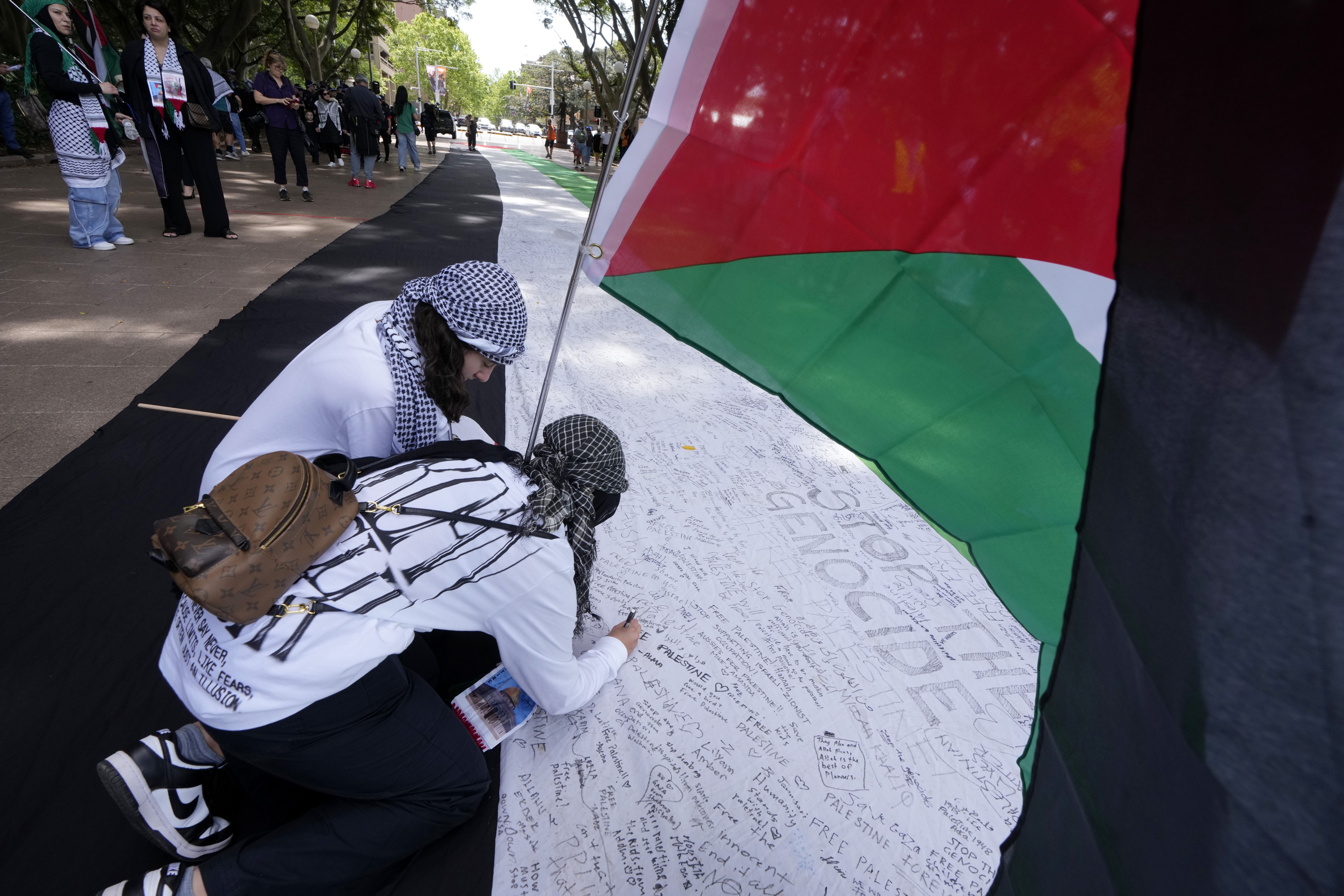 Two young women write on a giant flag as pro-Palestinian supporters rally in Sydney, Sunday, Oct. 6, 2024. (AP Photo/Rick Rycroft)