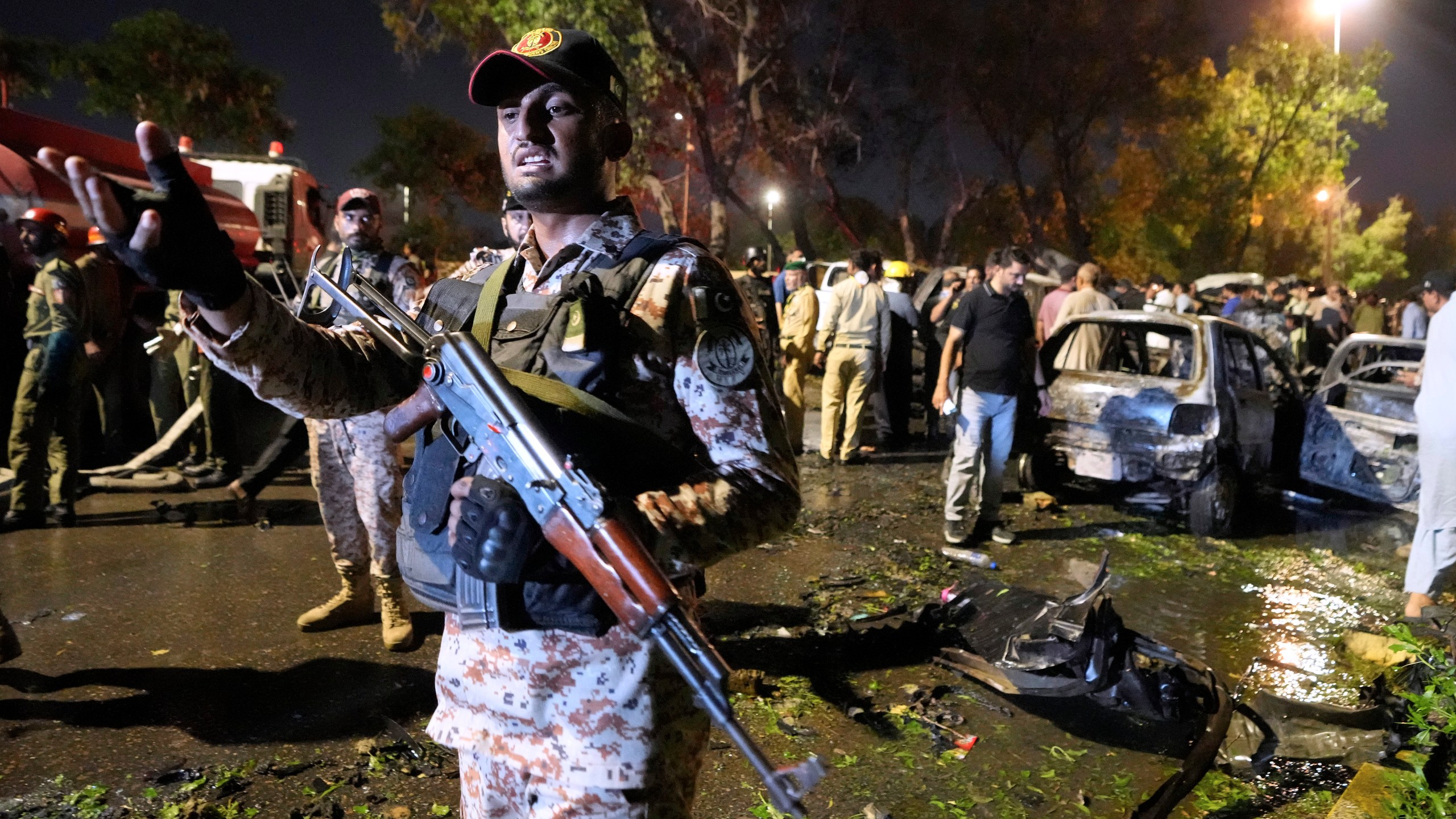 A paramilitary soldier gestures toward media as security officials examine the site of an explosion that caused injures and destroyed vehicles at outside the Karachi airport, Pakistan, Monday, Oct. 7, 2024. (AP Photo/Fareed Khan)