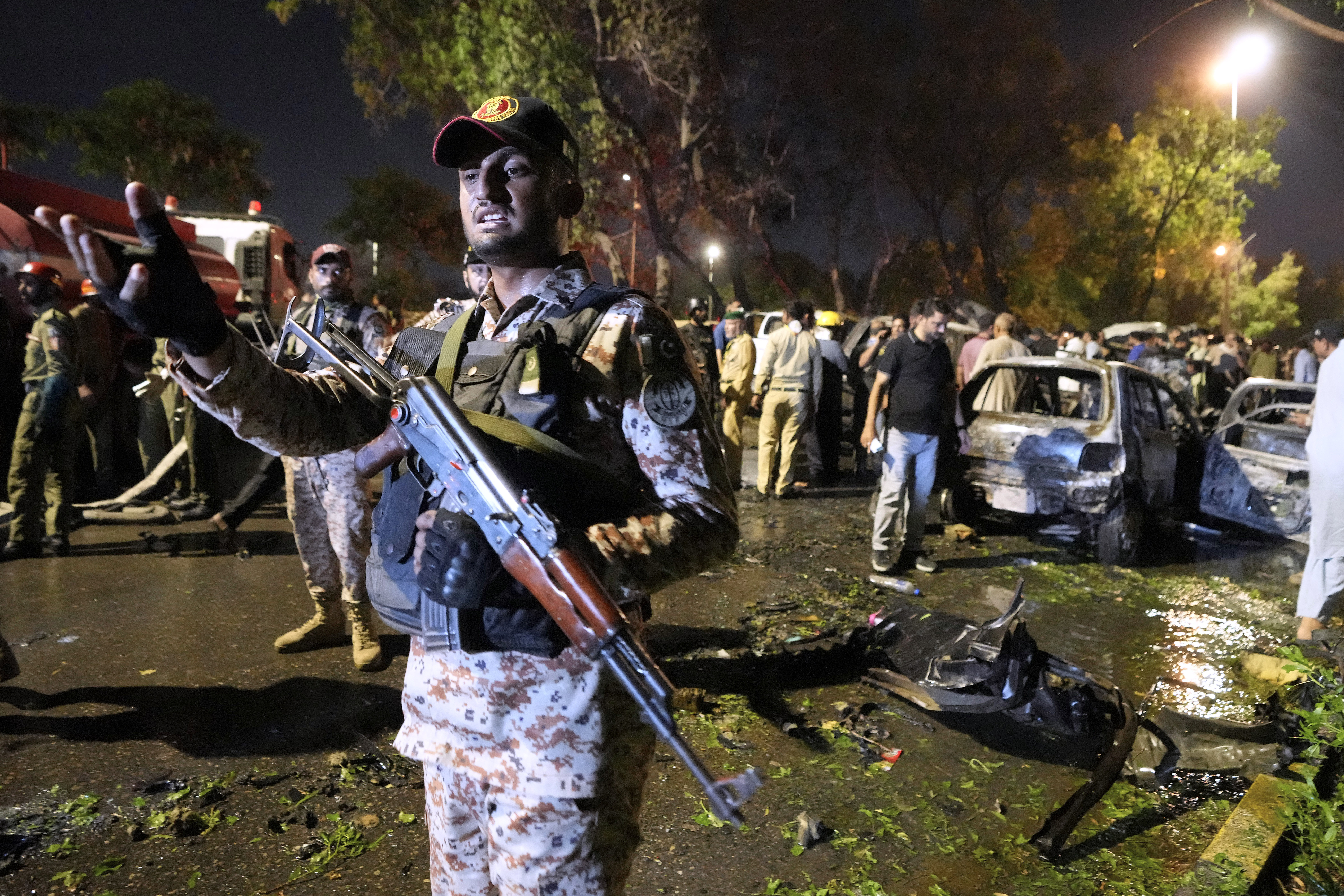 A paramilitary soldier gestures toward media as security officials examine the site of an explosion that caused injures and destroyed vehicles at outside the Karachi airport, Pakistan, Monday, Oct. 7, 2024. (AP Photo/Fareed Khan)