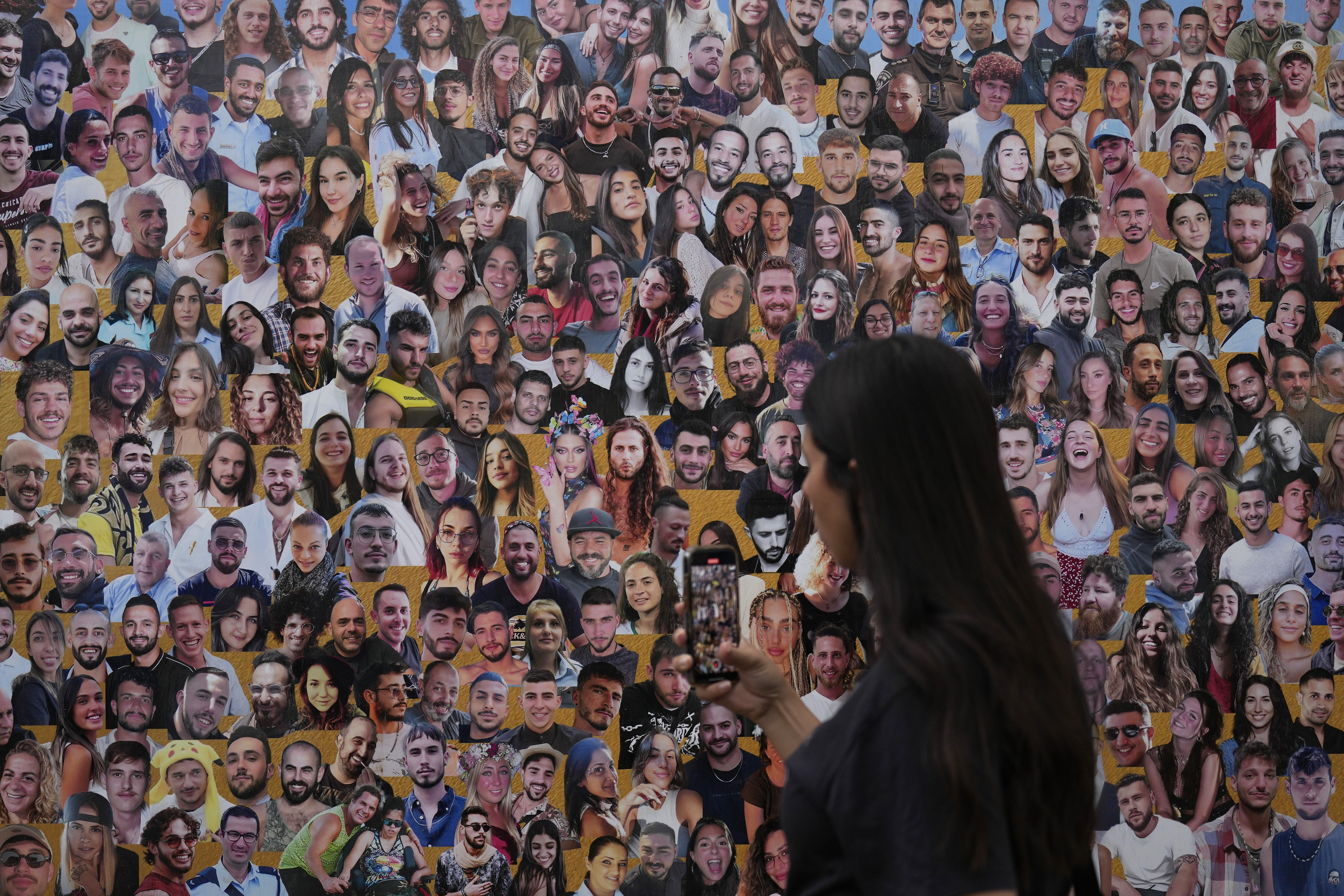 An attendant walks through a mural with portraits of the victims at the site of the Nova music festival, where hundreds of revelers were killed and abducted by Hamas and taken into Gaza, on the one-year anniversary of the attack, near Kibbutz Reim, southern Israel, Monday, Oct. 7, 2024. (AP Photo/Ariel Schalit)