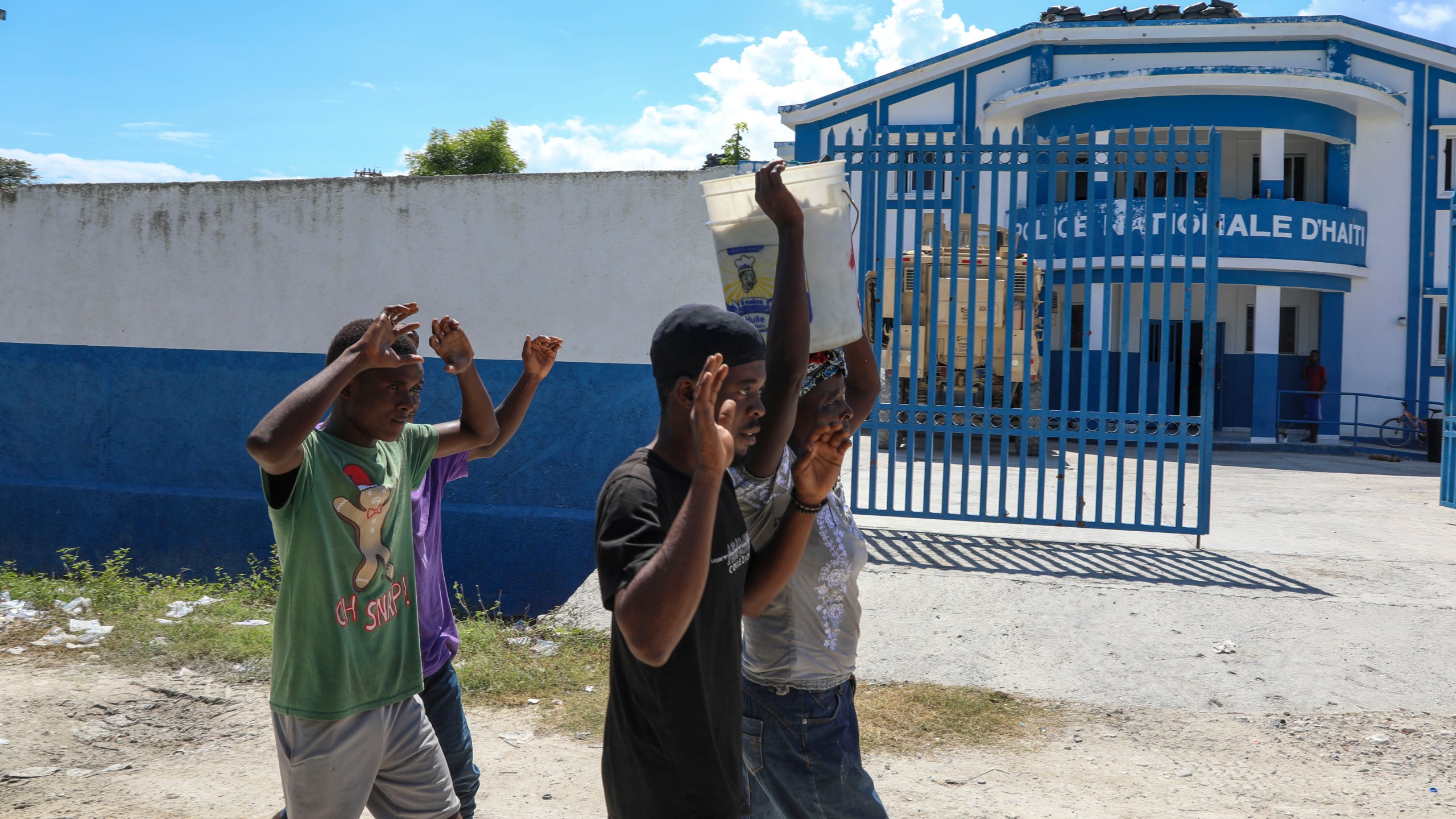 People raise their arms while walking past a police station in Pont-Sonde, Haiti, Monday, Oct. 7, 2024, days after a gang attacked the town. (AP Photo/Odelyn Joseph)