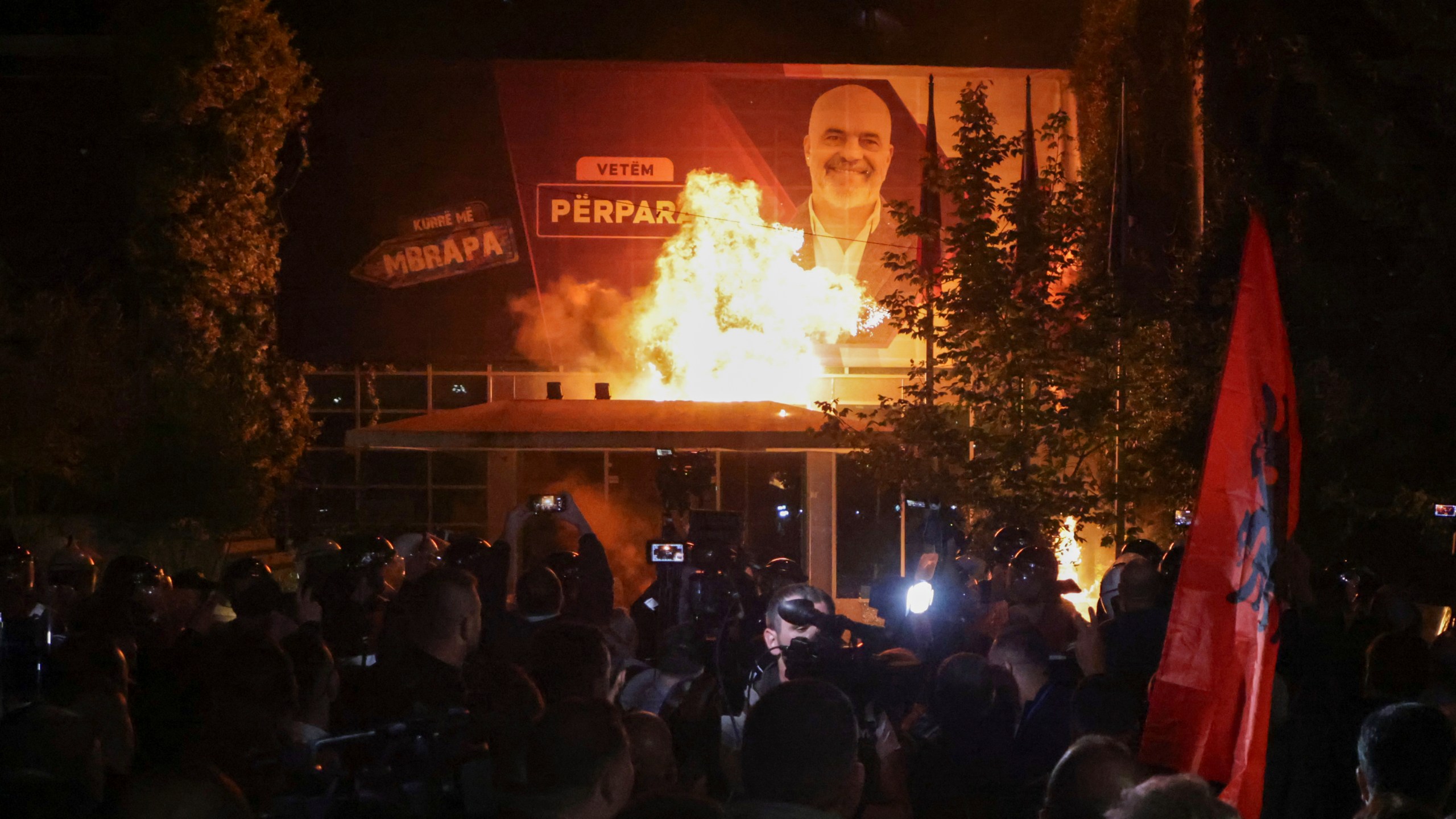 Fire burns behind a riot police cordon and in front of a poster depicting the Albania Prime minister Edi Rama during an anti-government rally set up by the opposition, in Tirana, Albania, Monday, Oct. 7, 2024. (AP Photo/Hameraldi Agolli)