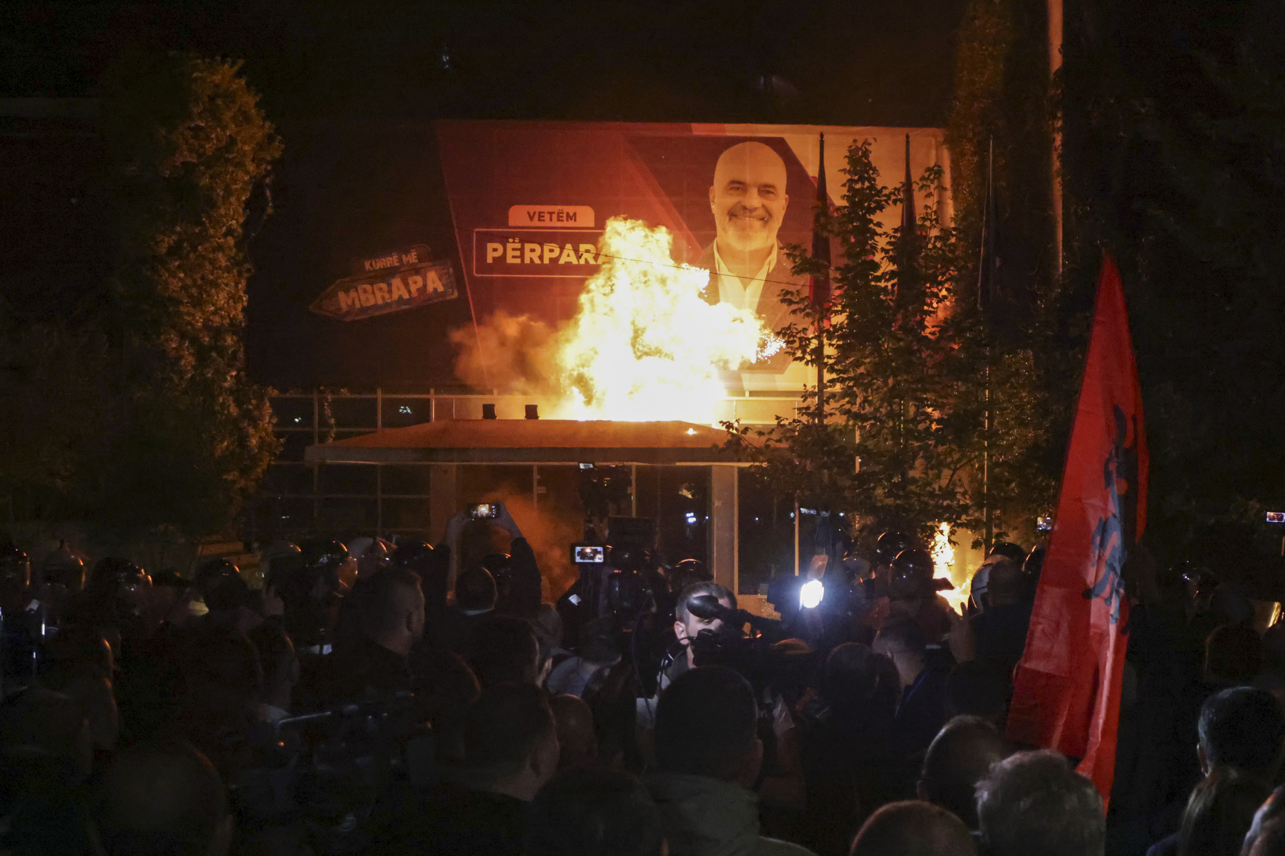 Fire burns behind a riot police cordon and in front of a poster depicting the Albania Prime minister Edi Rama during an anti-government rally set up by the opposition, in Tirana, Albania, Monday, Oct. 7, 2024. (AP Photo/Hameraldi Agolli)