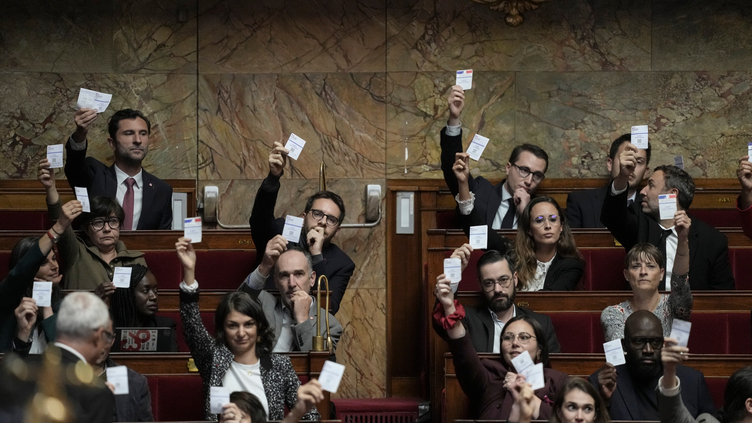 Members of the French unbowed party show their voting cards during the speech Prime Minister Michel Barnier arrives at the National Assembly, in Paris, Tuesday, Oct. 1, 2024. (AP Photo/Thibault Camus)