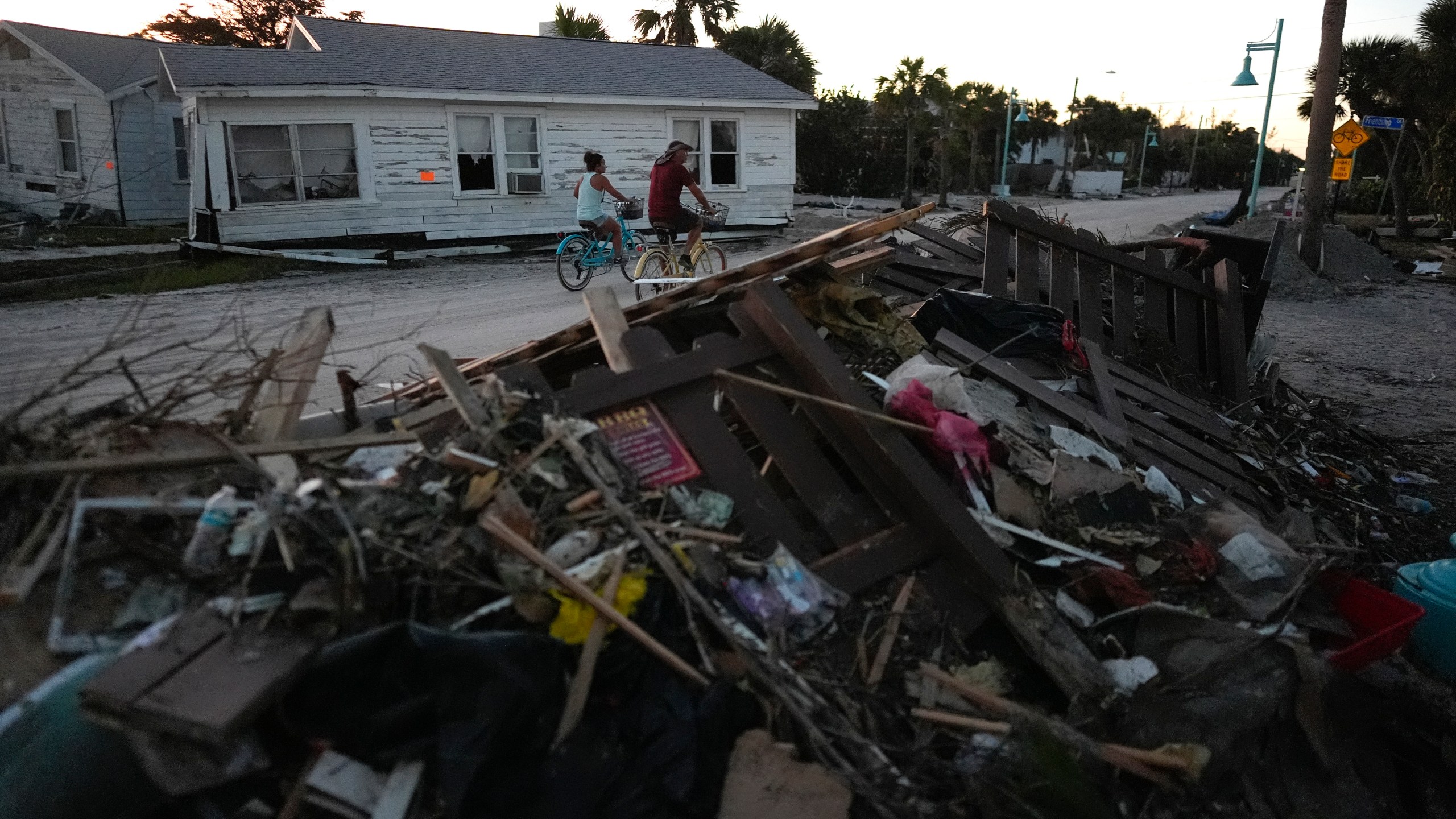 FILE - People bike past damaged homes and debris left by Hurricane Milton, on the sand-coated main road of southern Manasota Key, already cleared of feet of sand, in Englewood, Fla., Oct. 13, 2024. (AP Photo/Rebecca Blackwell, File)