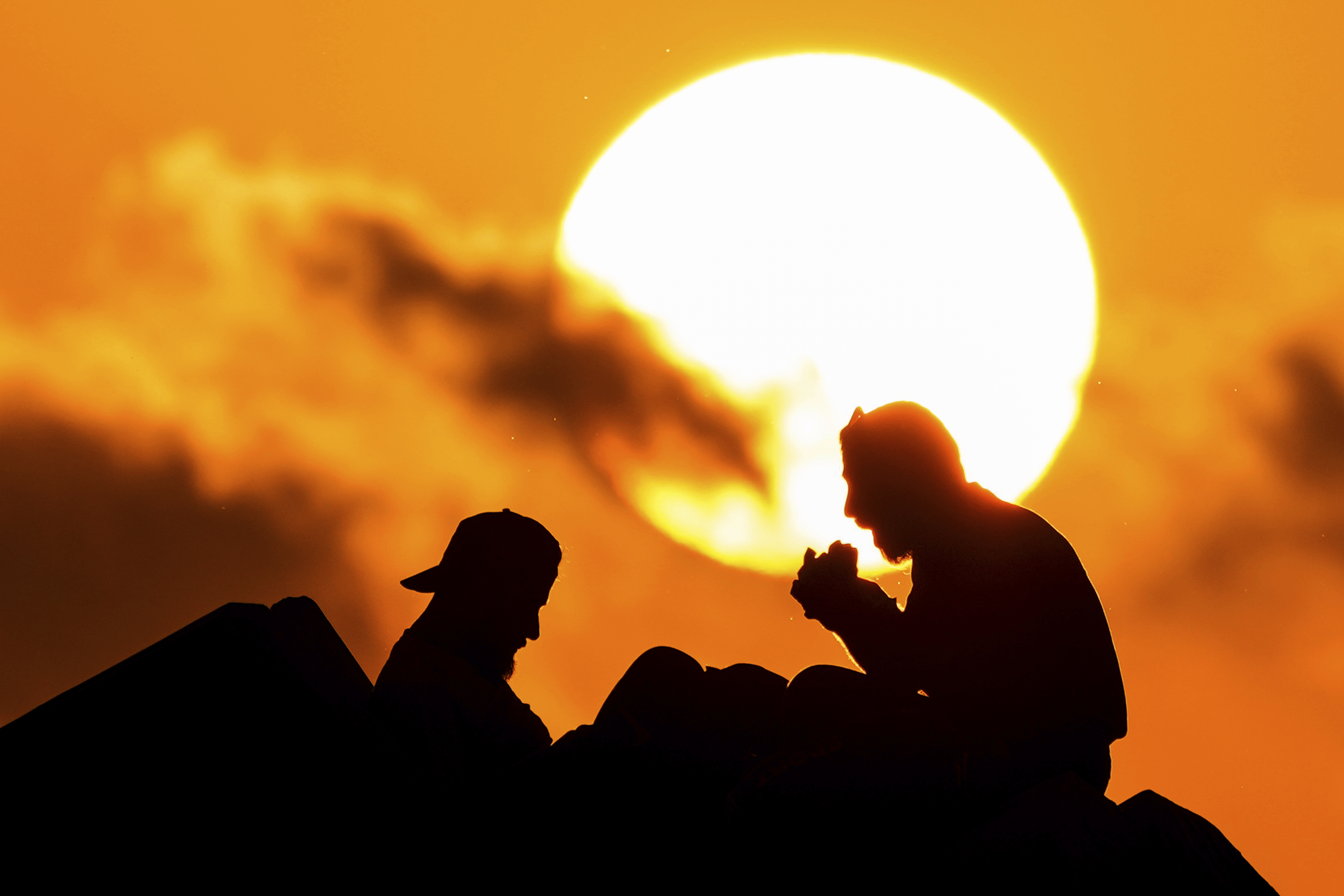 Displaced men fleeing the Israeli airstrikes in Beirut's Dahiyeh suburb, eat as sit at Beirut's seaside promenade, along the Mediterranean Sea while the sun sets over the capital Beirut, Lebanon, Thursday, Oct. 17, 2024. (AP Photo/Hassan Ammar)