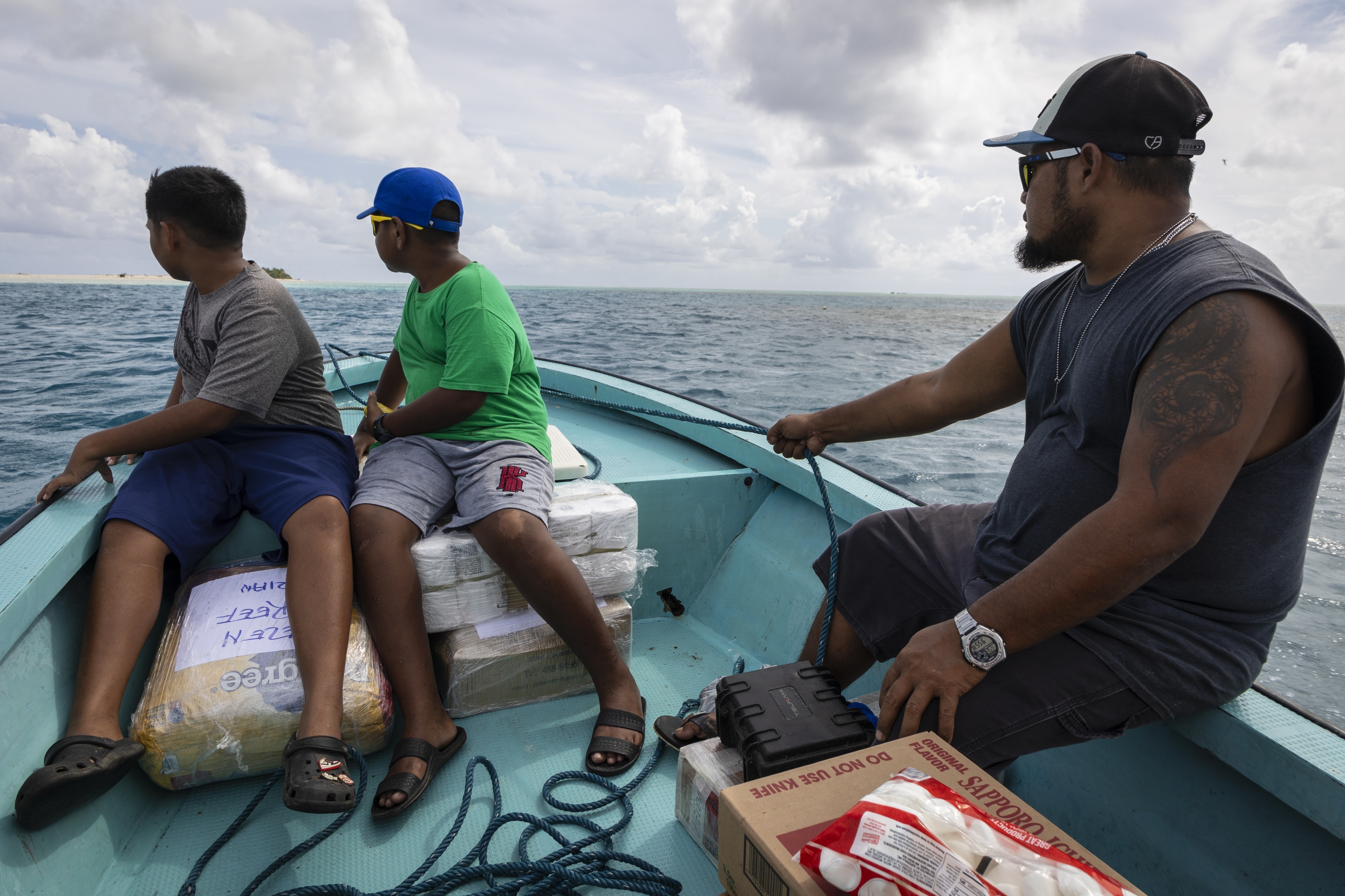 Metfidza Marino, from left, Aarson Aaron and Aaron Cyrillo look out to Helen Island, Palau, as a small speed boat transports toilet paper, dog food and other goods to the remote atoll on July 17, 2024. (AP Photo/Yannick Peterhans)