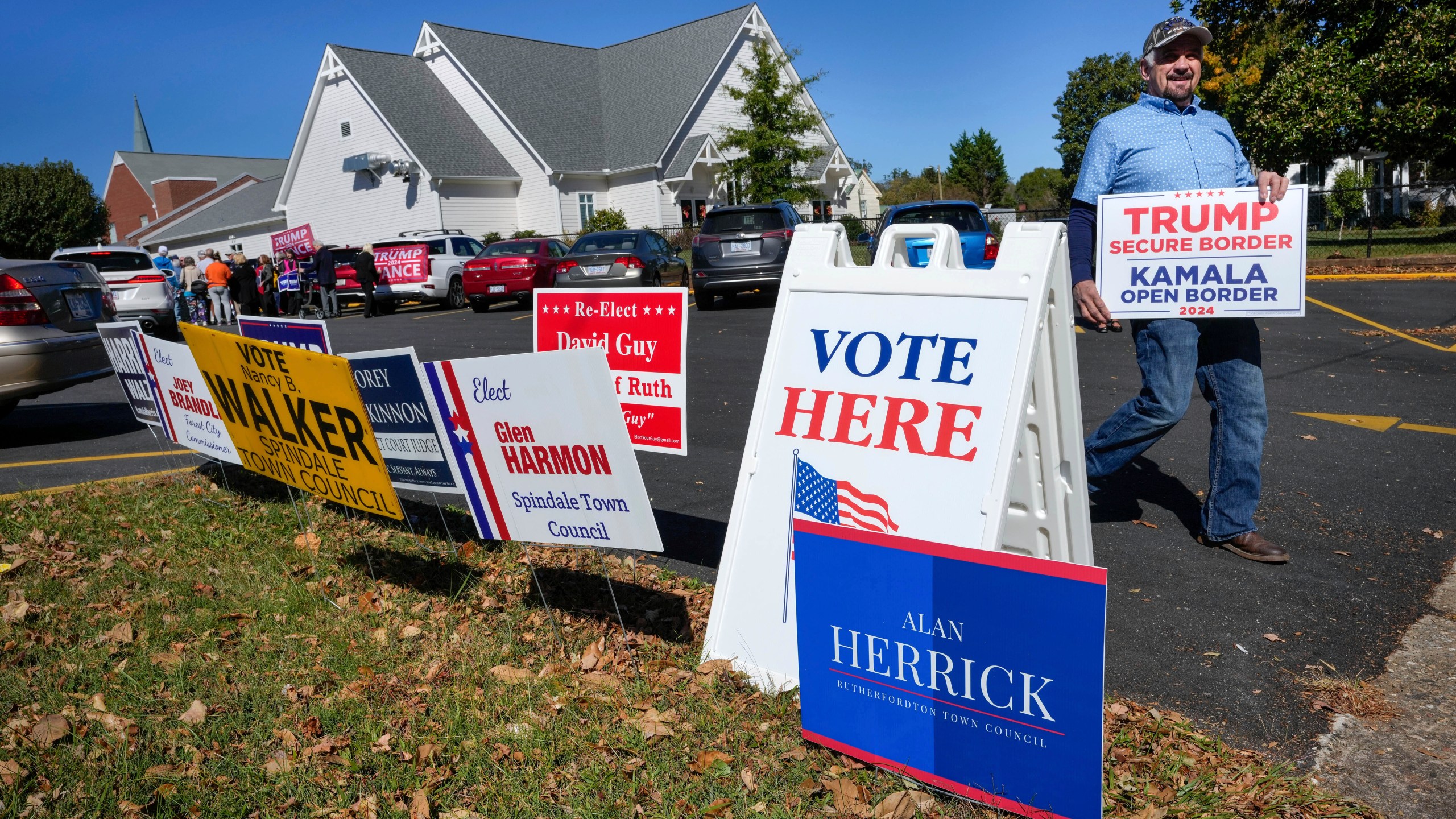 A supporter for former President Trump walks past political signs outside the Rutherford County Annex Building, an early voting site, Thursday, Oct. 17, 2024 in Rutherfordton, N.C. (AP Photo/Kathy Kmonicek)